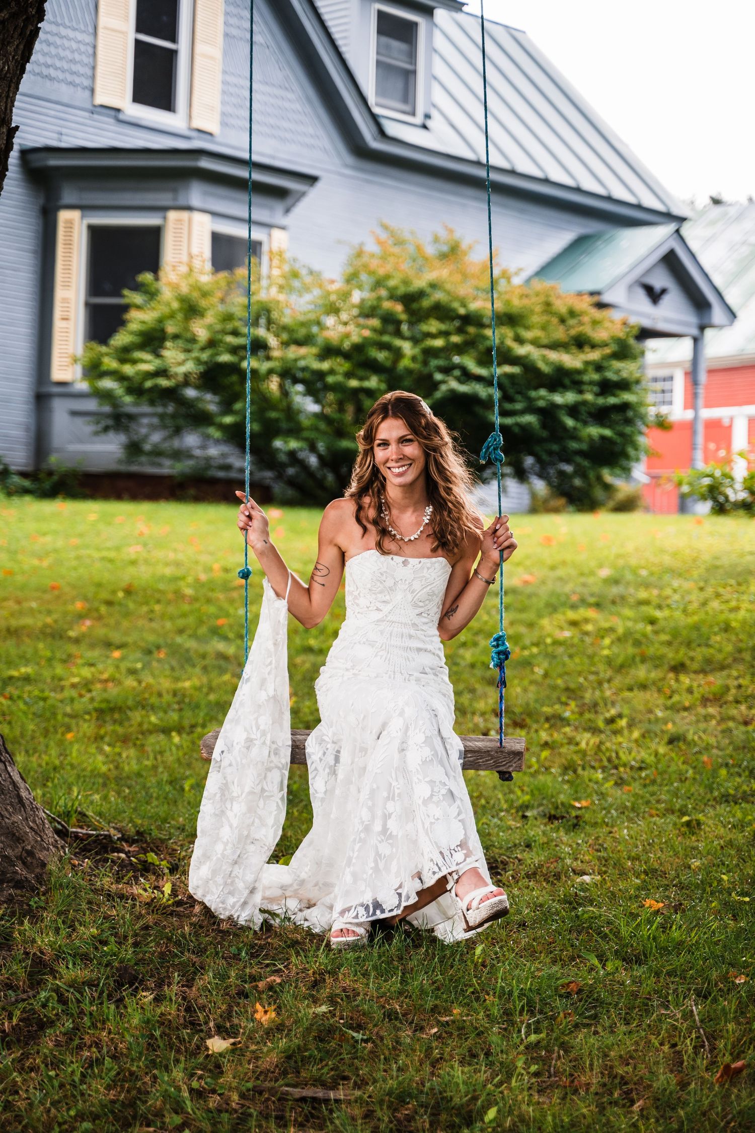 A lace wedding dress worn on a swing in front of a blue house with white trim.