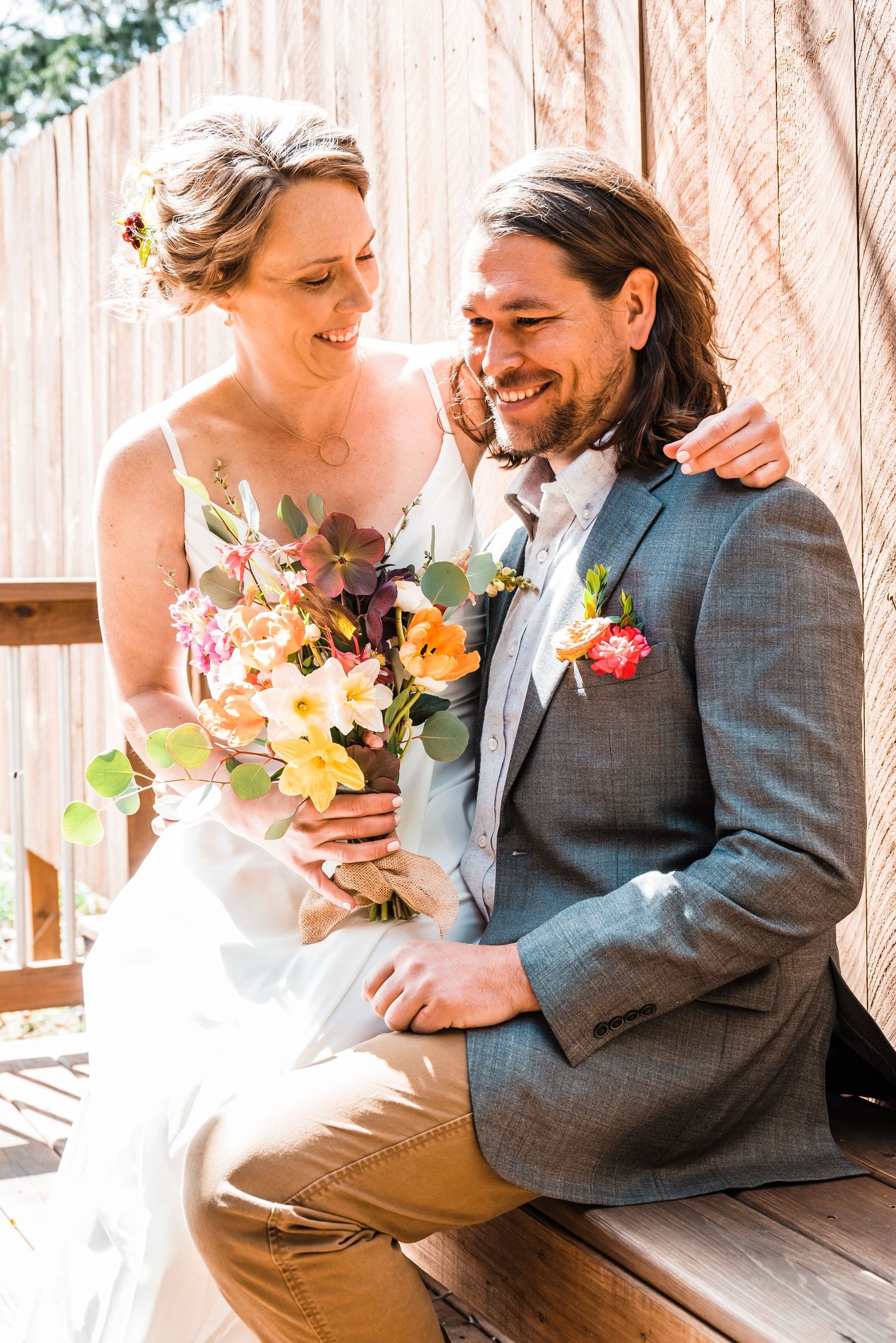 Joyful couple laughing together on wooden bench with bright floral bouquet.