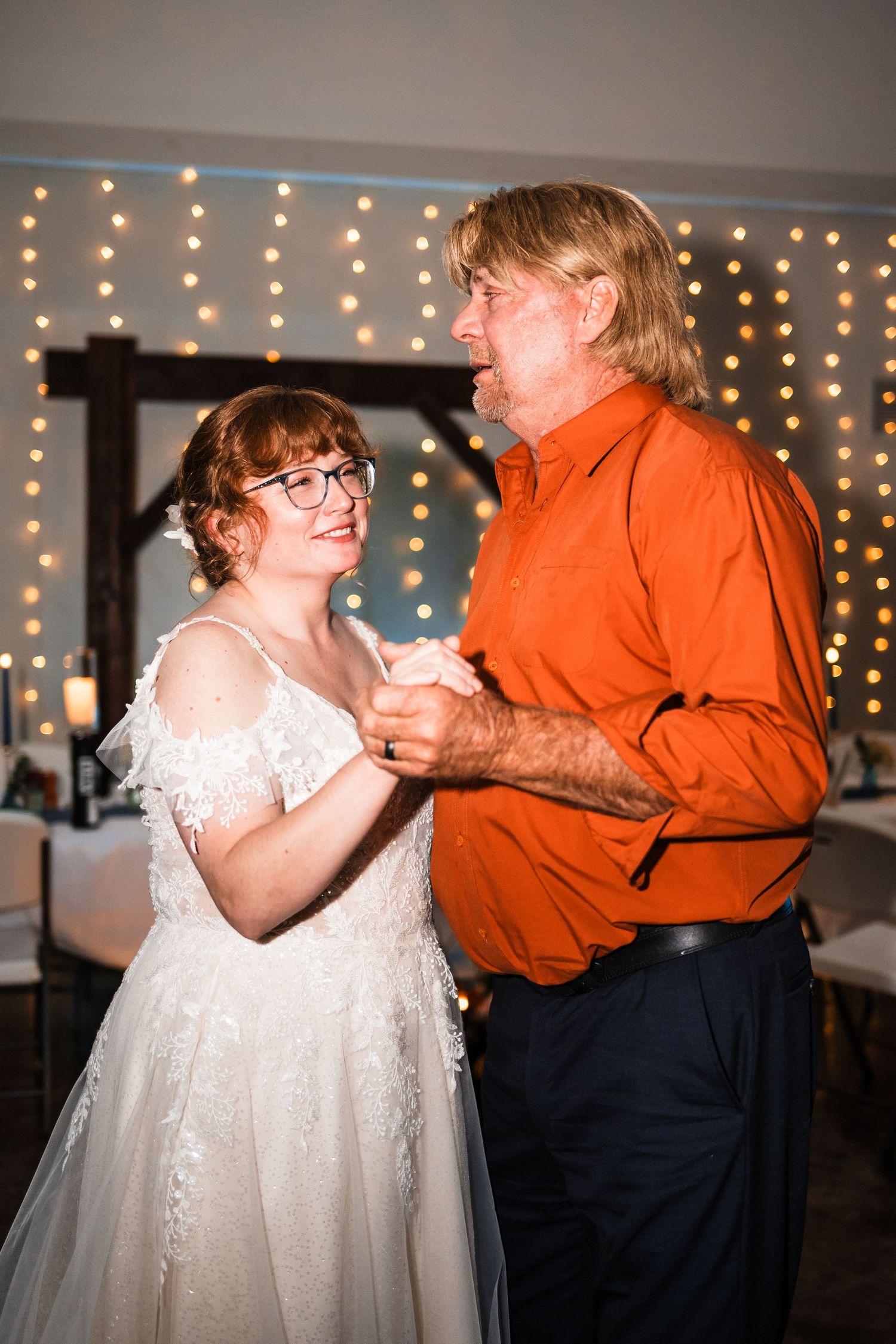 A tender dance moment between two people at a wedding reception with twinkle lights.