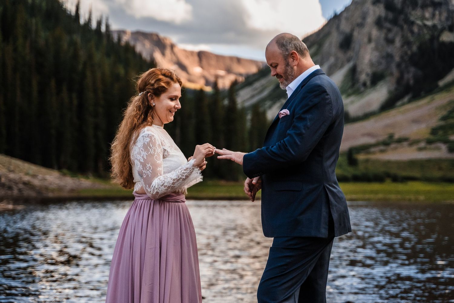 Couple exchanging rings during an intimate mountain lakeside ceremony in a stunning natural setting.