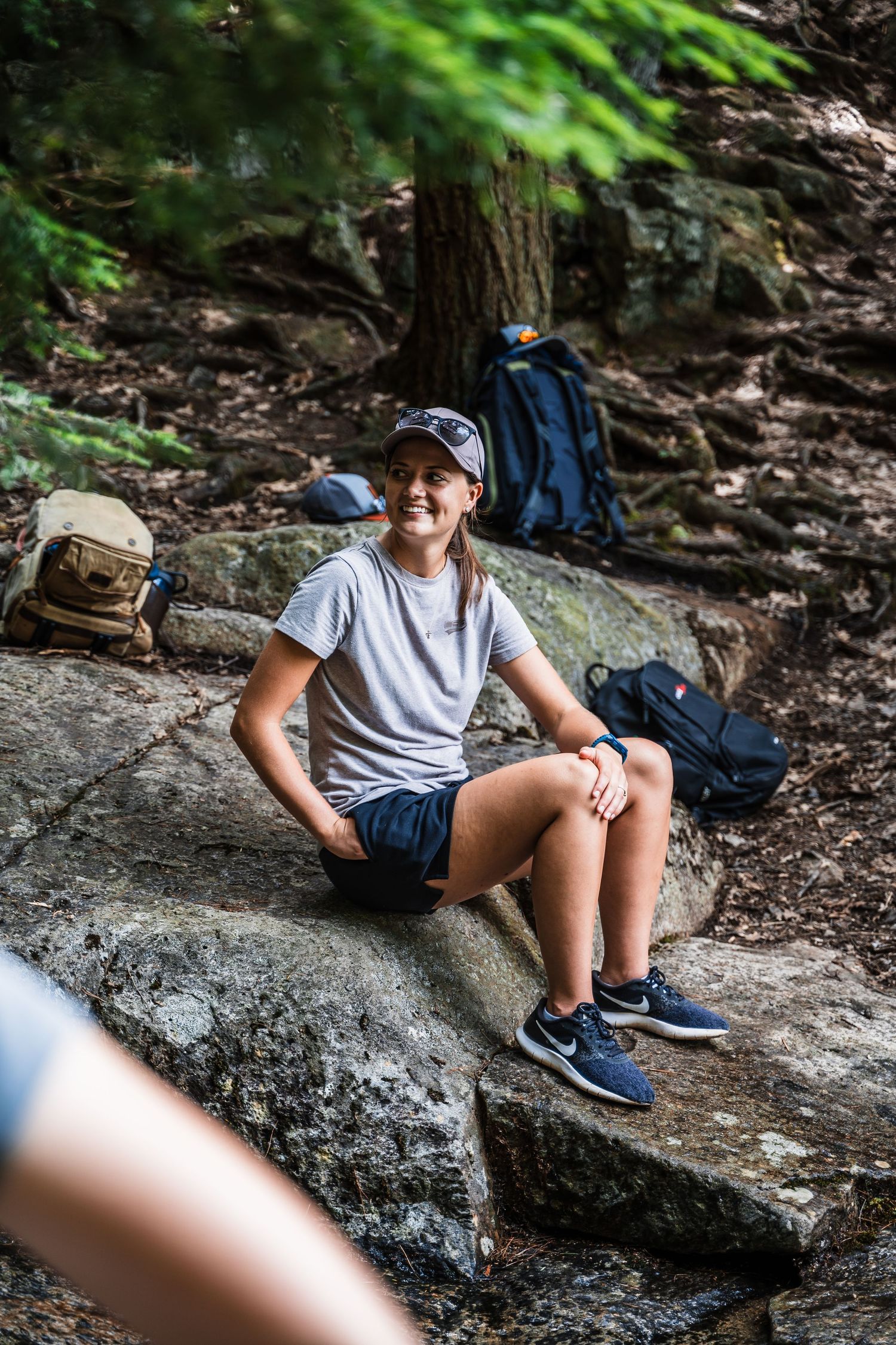 Hiker rests on a rocky outcrop surrounded by backpacks and forest greenery.