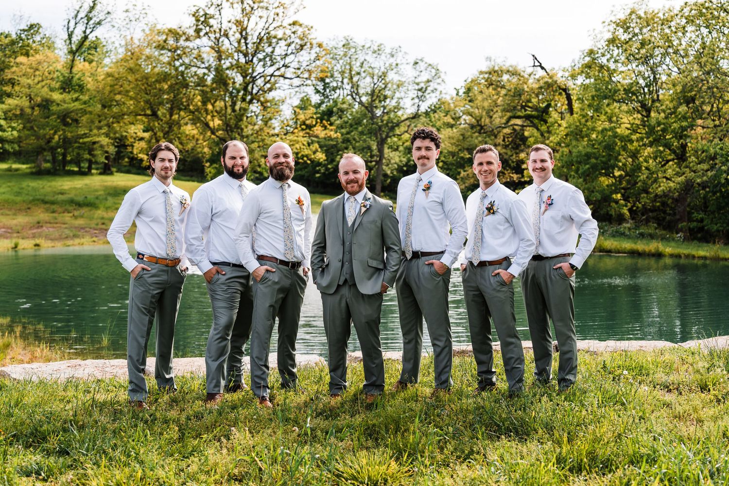 Groom and groomsmen pose together in gray suits by a serene pond.