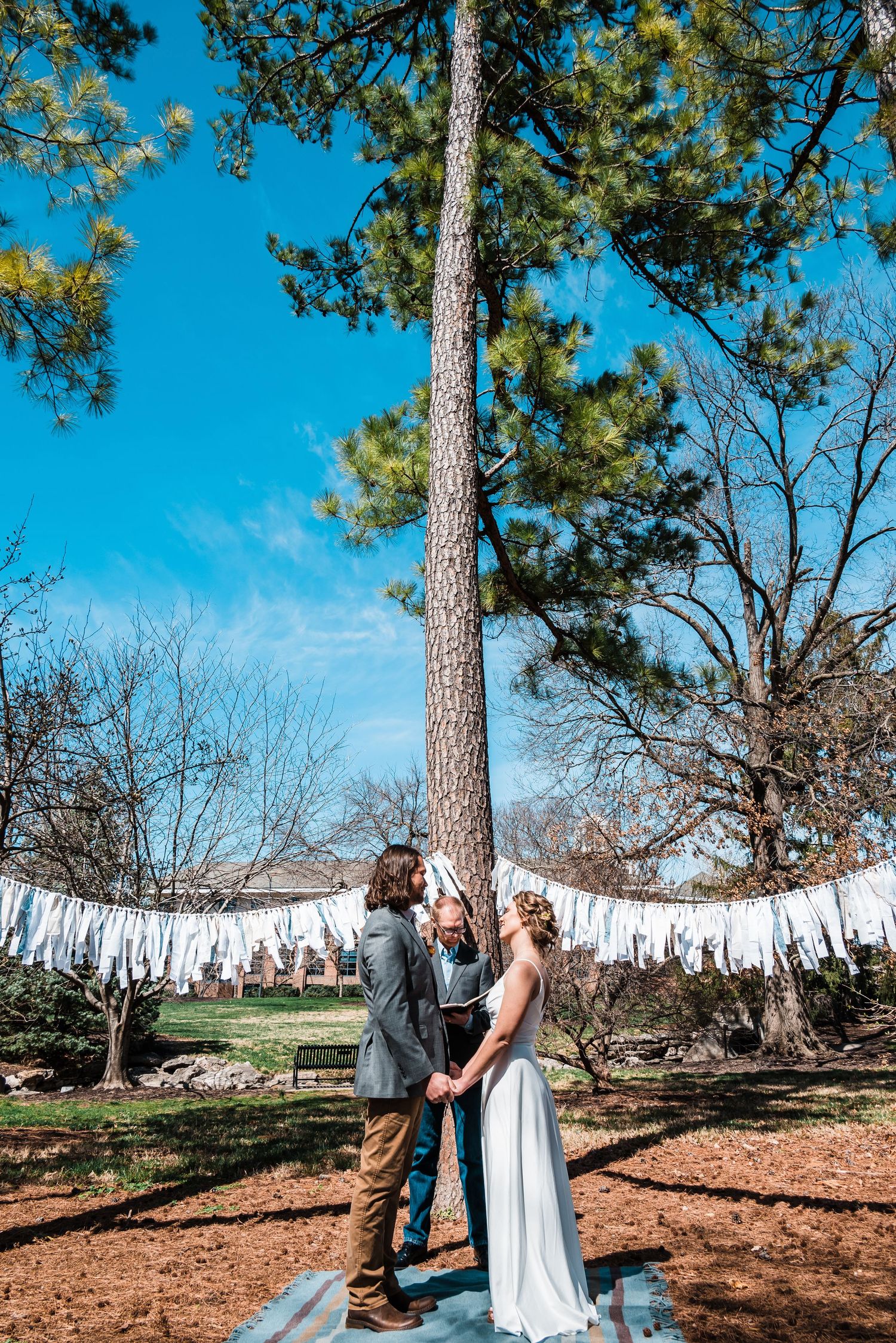 A couple sharing an intimate moment under pine trees decorated with white fabric streamers.