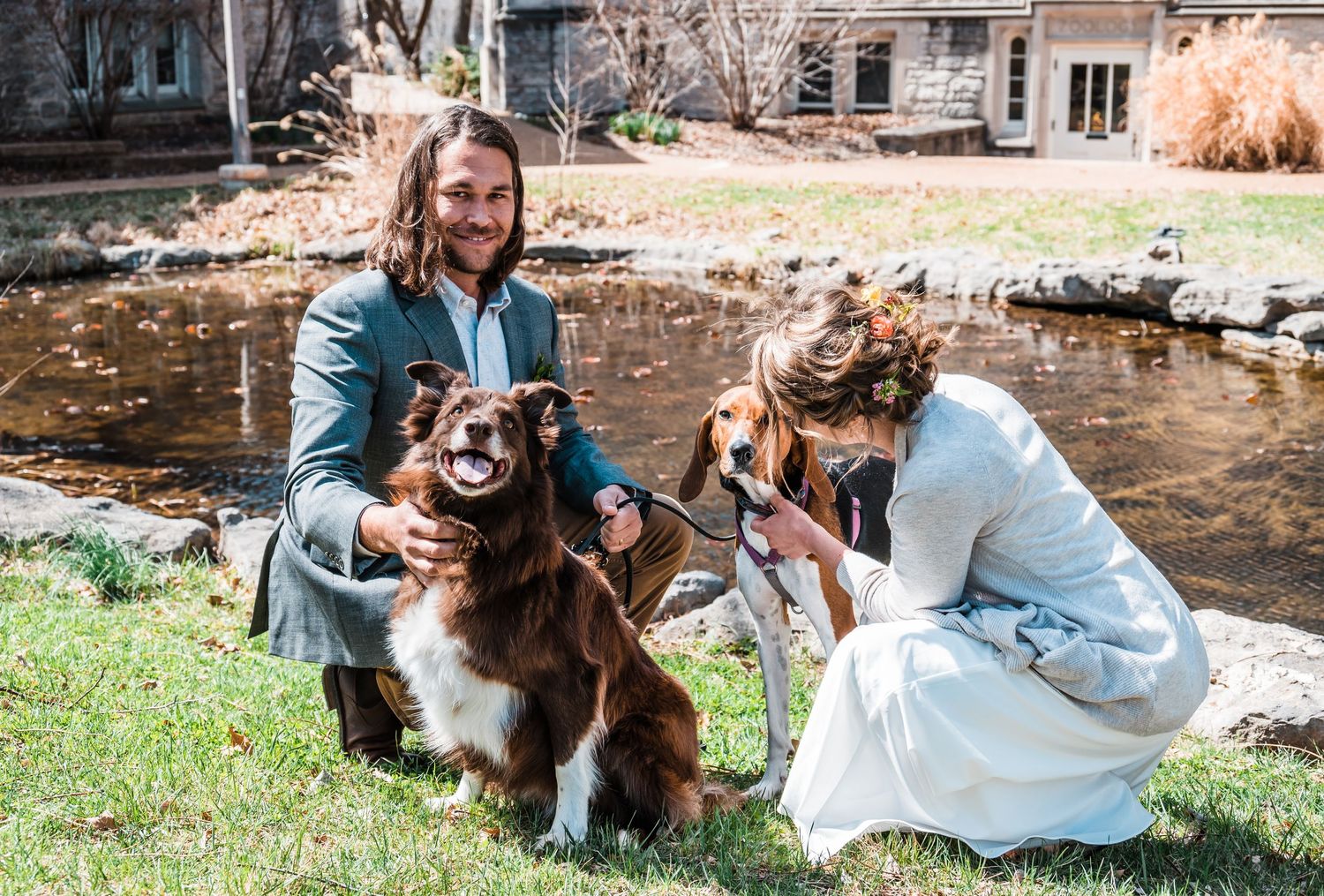 Wedding couple posing with their two dogs by pond in garden setting.