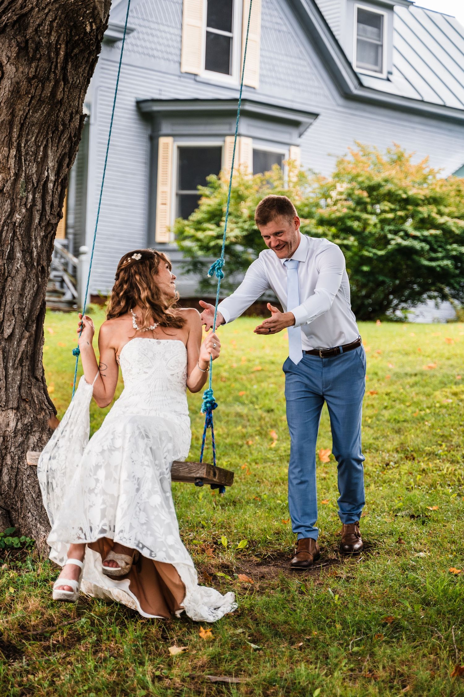 A couple sharing a playful moment on a tree swing in a garden setting.