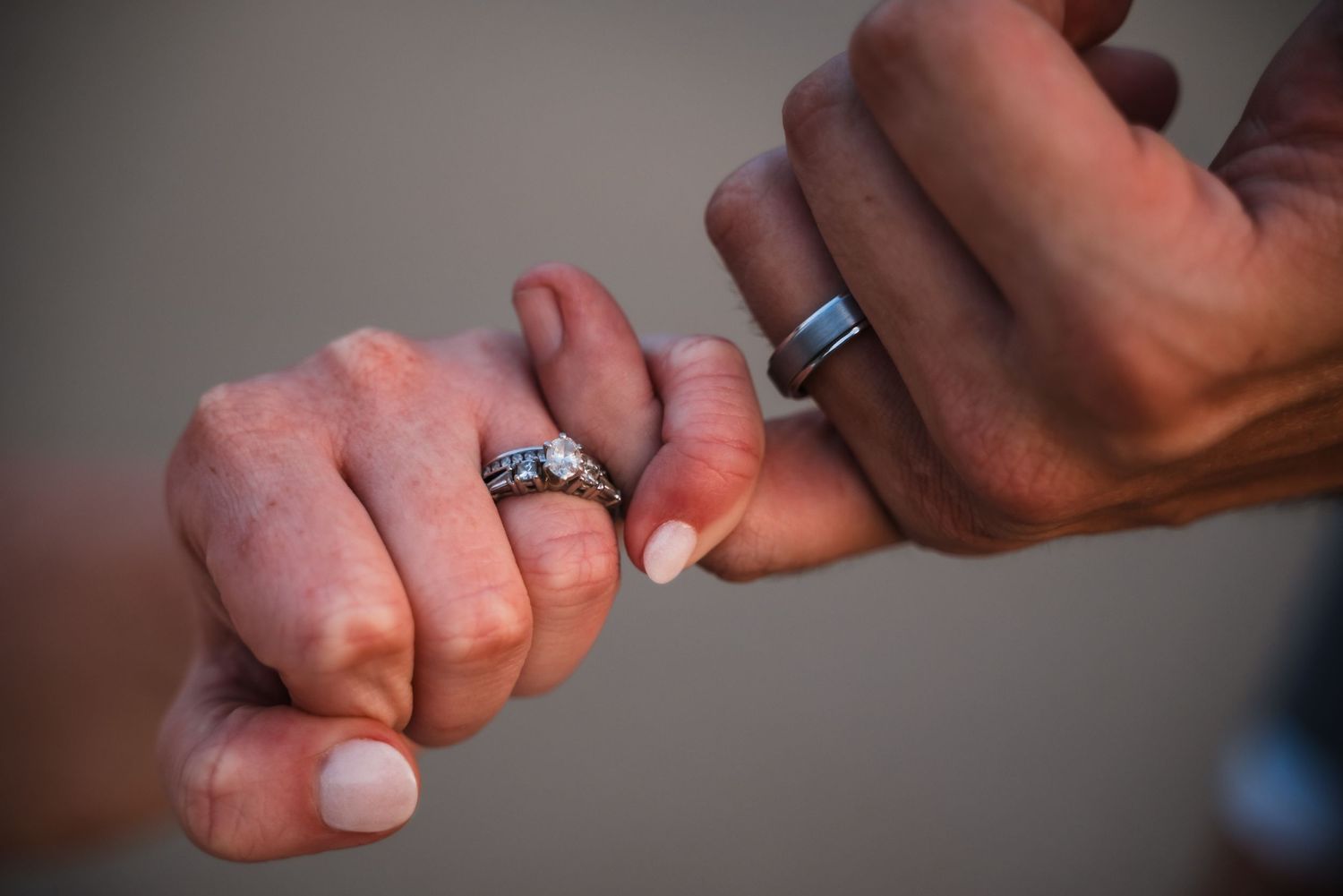Close-up of two hands with wedding rings touching pinky fingers together.
