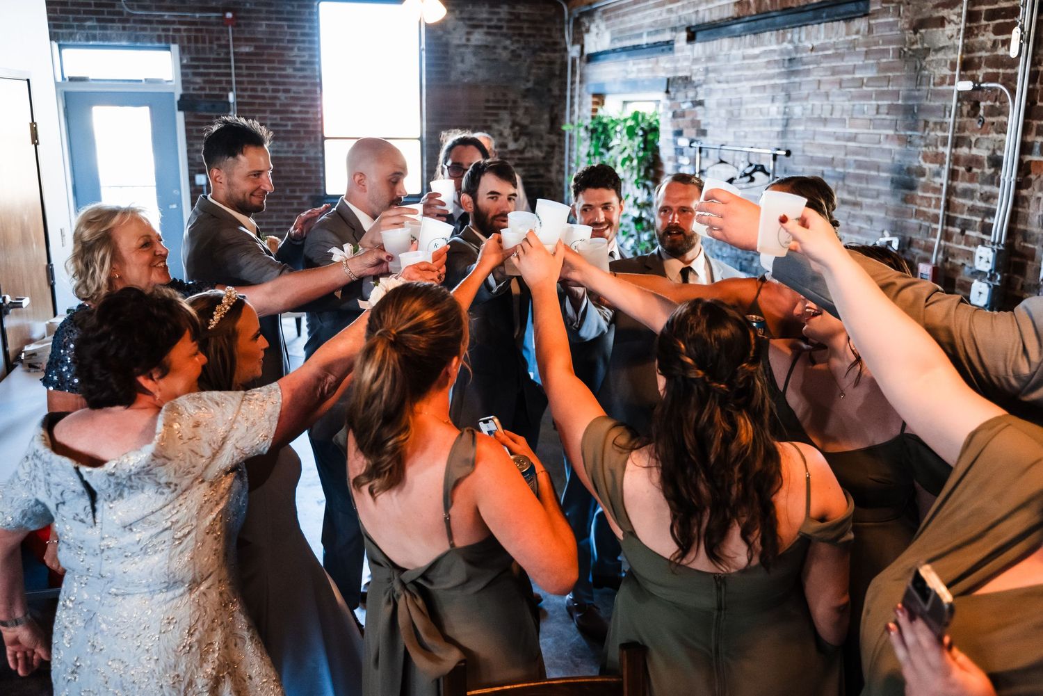 A group of friends raise their glasses together in a celebratory toast inside a rustic brick venue.