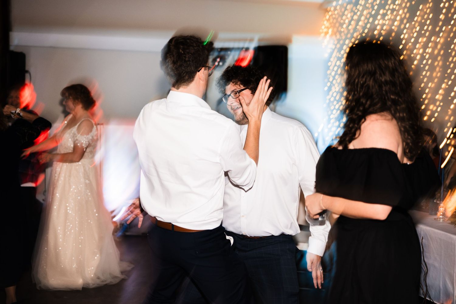 Wedding reception guests dance energetically under sparkling fairy lights at an indoor venue.