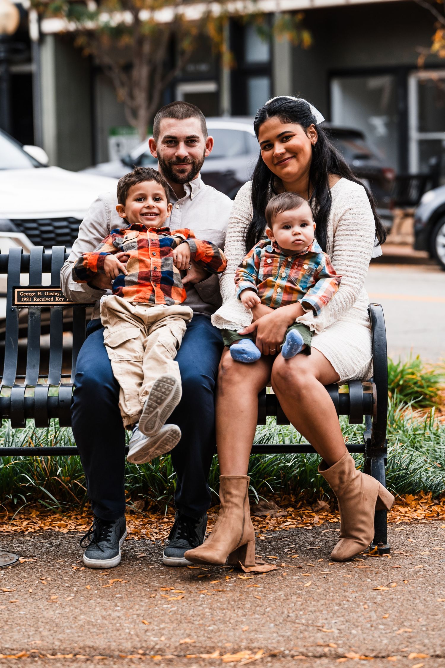 Family sitting together on park bench during autumn with toddlers in matching outfits.