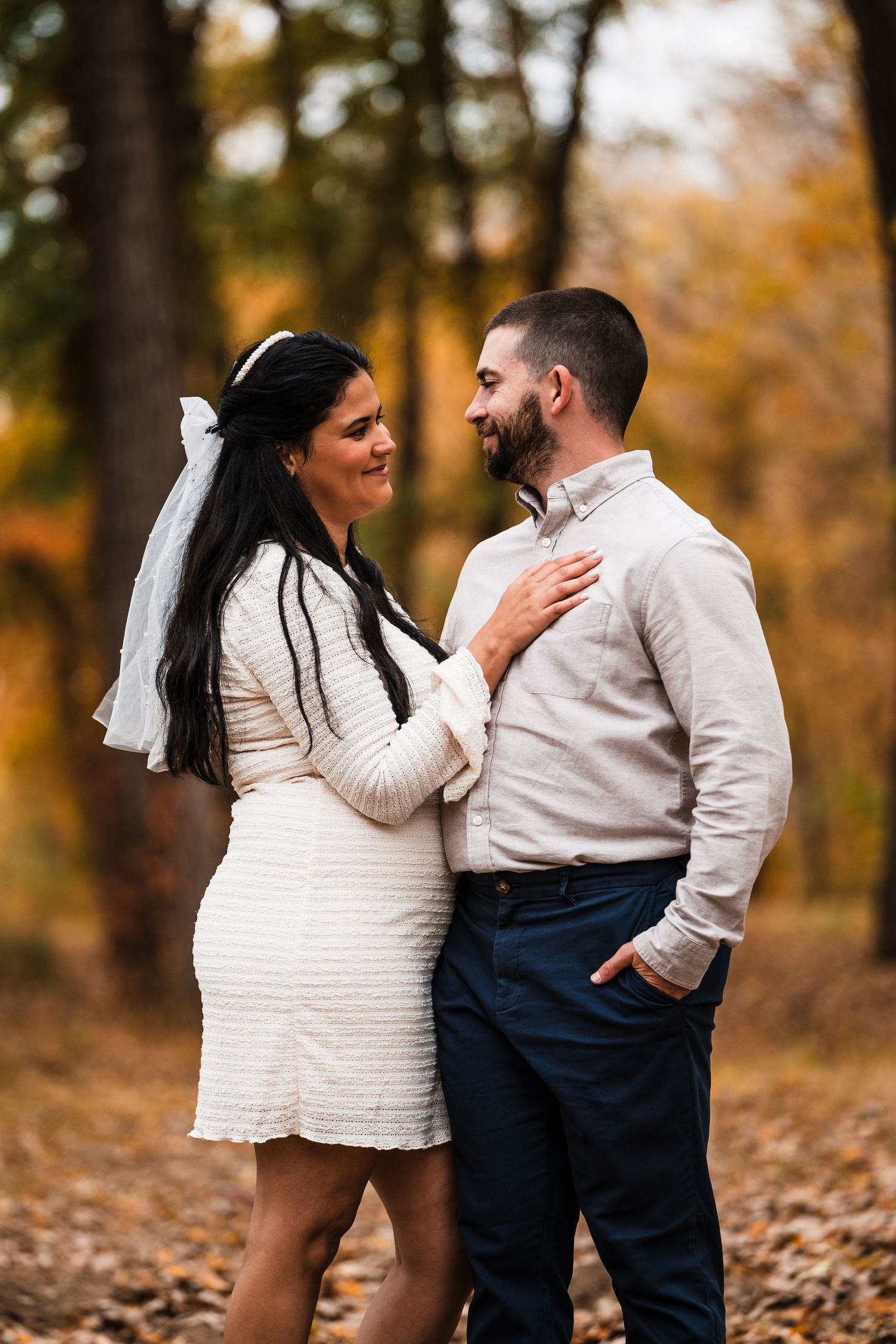 Romantic couple embracing outdoors with fall foliage in background.
