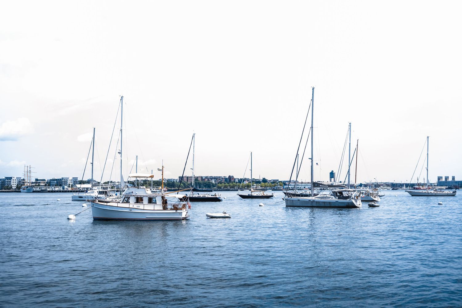 Sailboats and yachts anchored in a calm harbor on a cloudy day.
