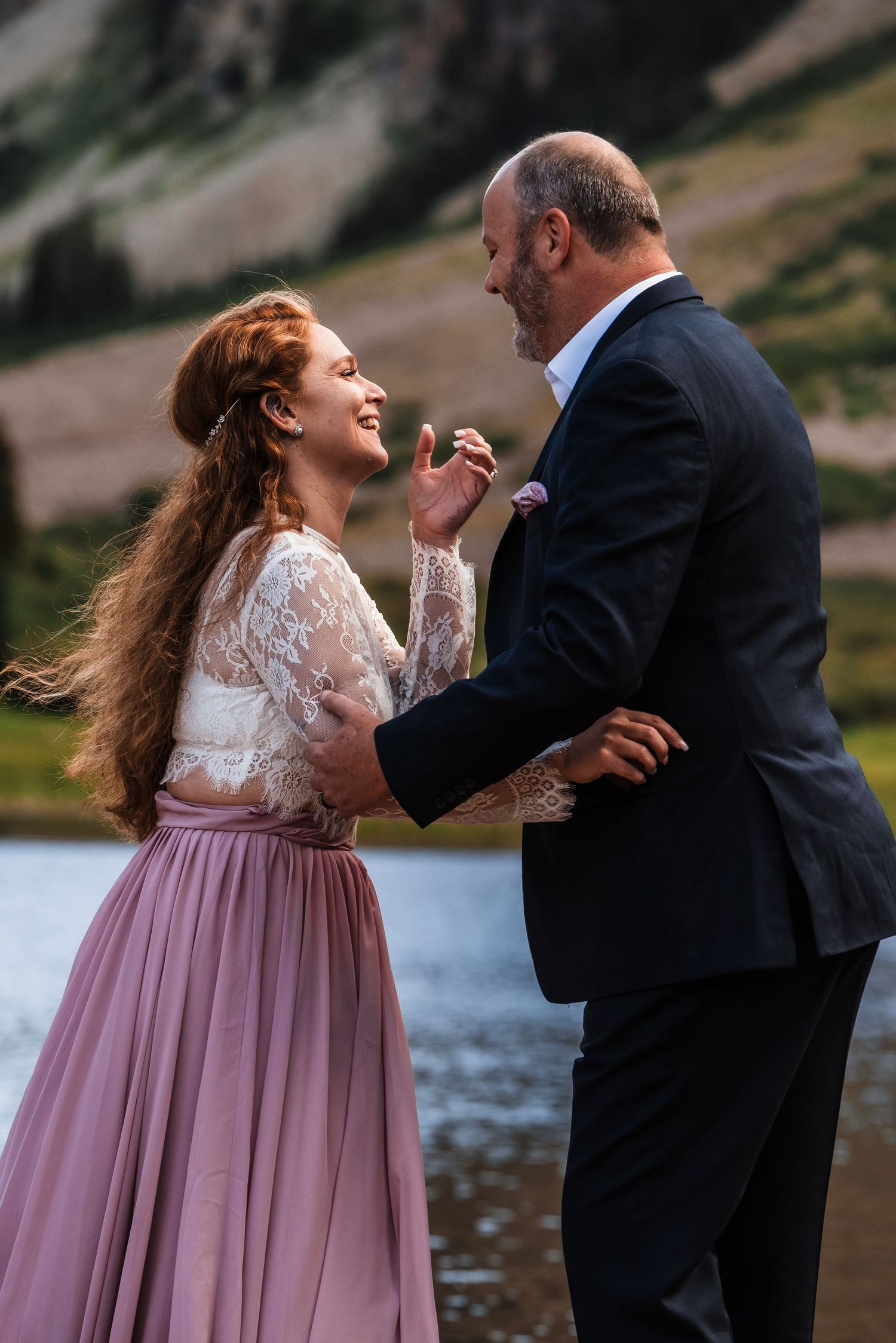 Happy couple sharing a joyful moment by an alpine lake with dramatic mountain backdrop.
