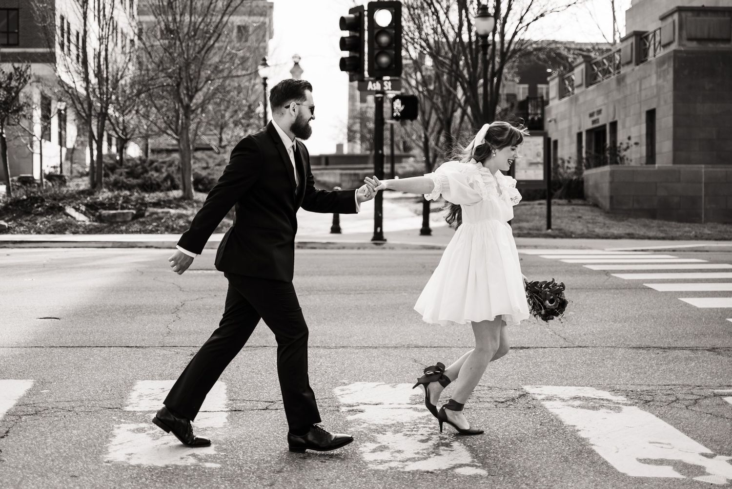 A couple and their dog cross an urban street intersection during a wedding photoshoot.
