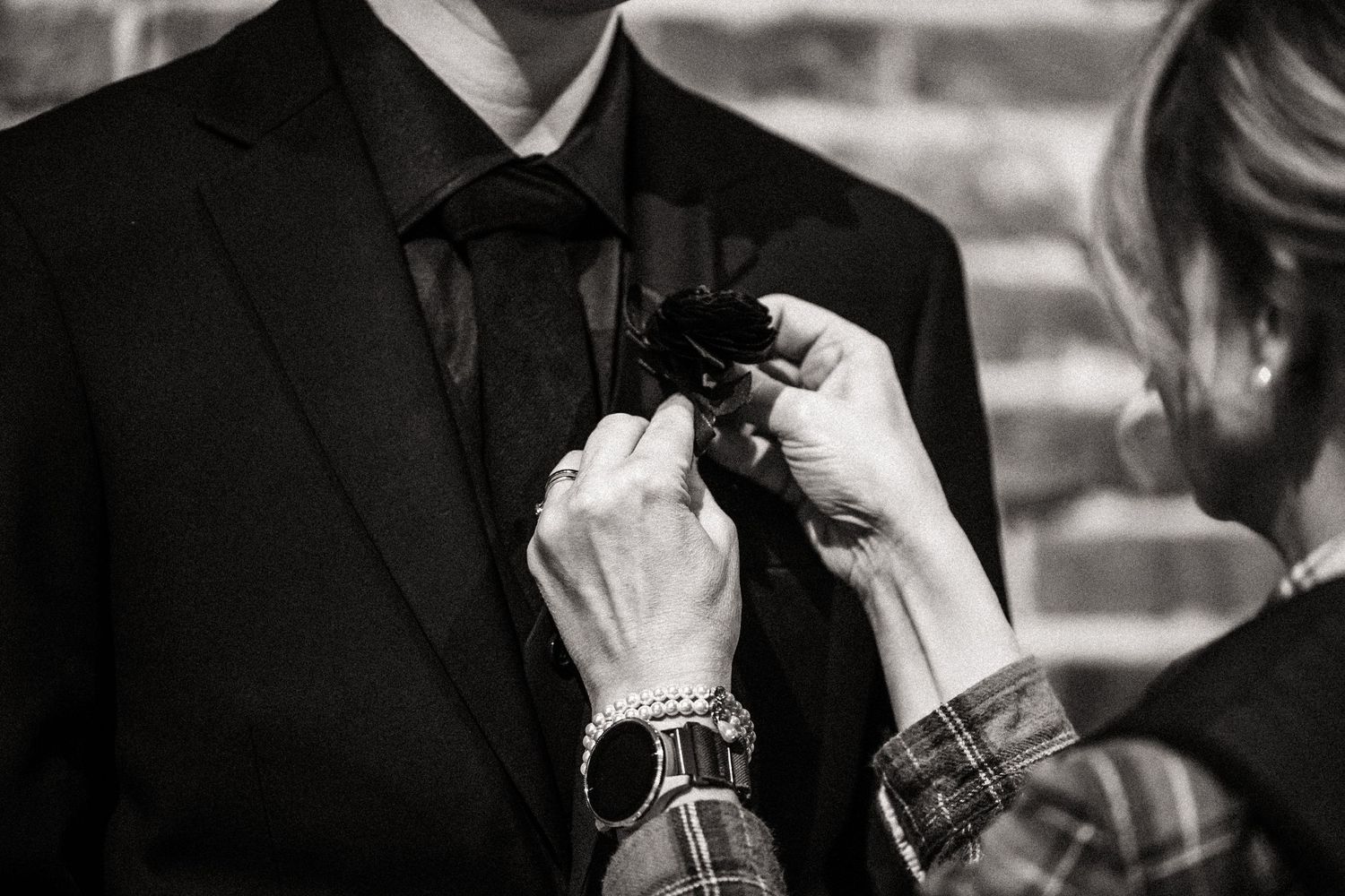 Close-up shot of hands adjusting a boutonniere on a black suit jacket.