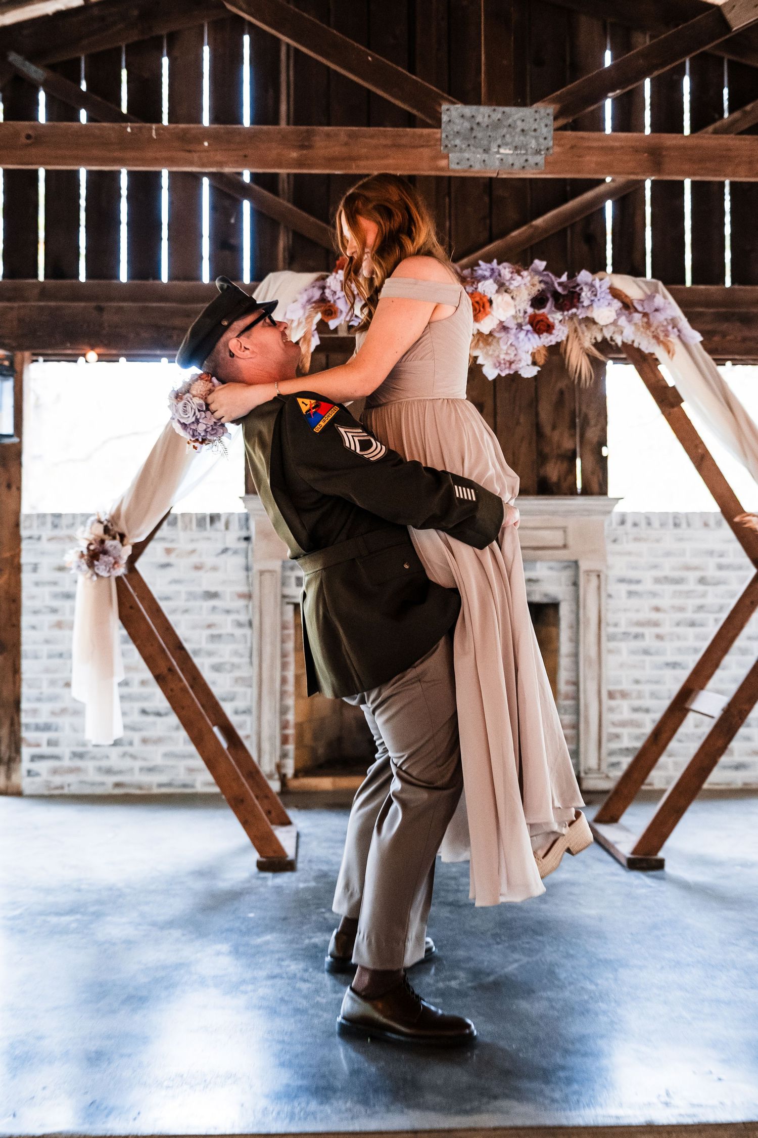 Romantic couple dancing and dipping in a rustic barn venue with wooden beams overhead.