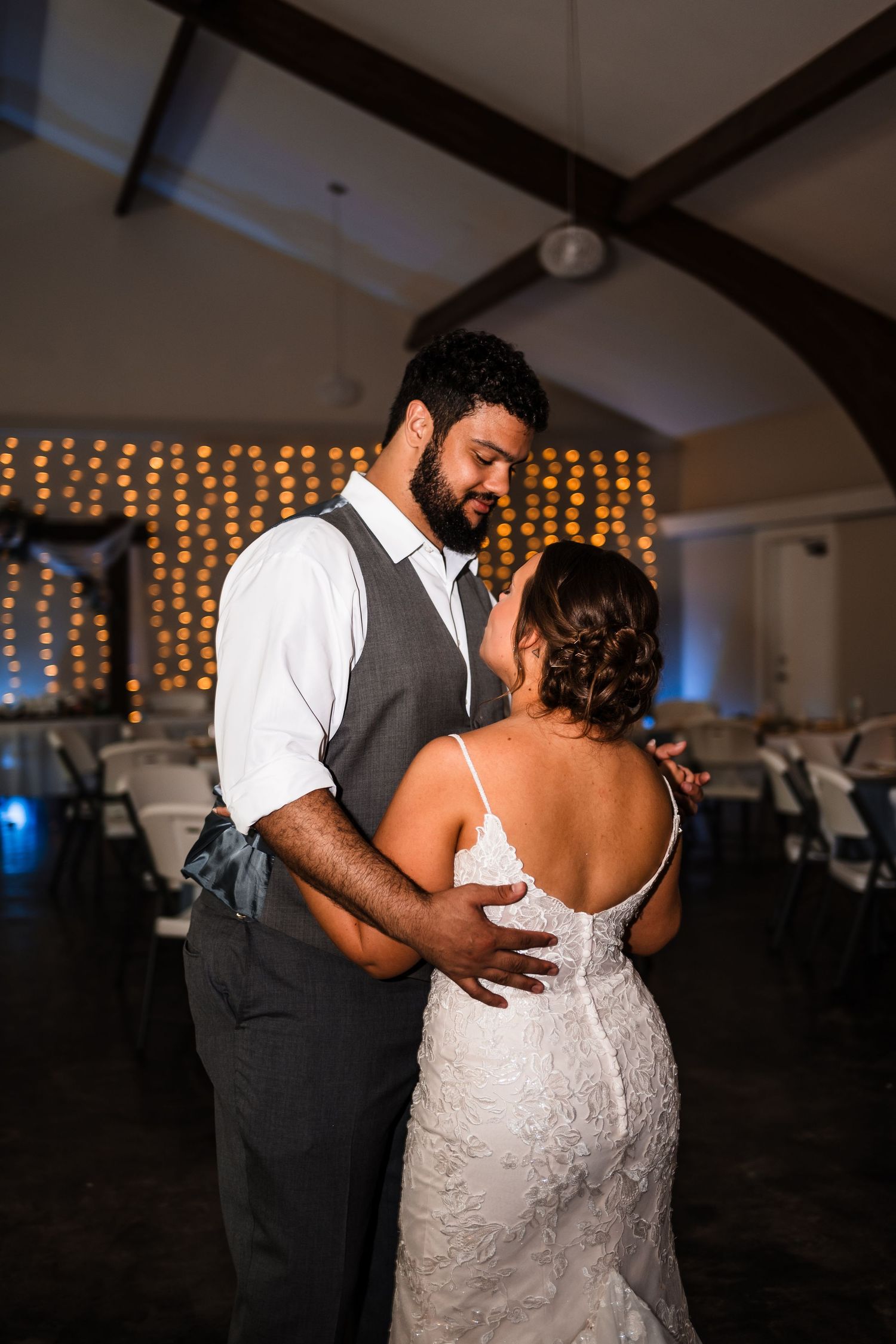 A couple shares an intimate dance moment at their wedding reception with string lights glowing in the background.