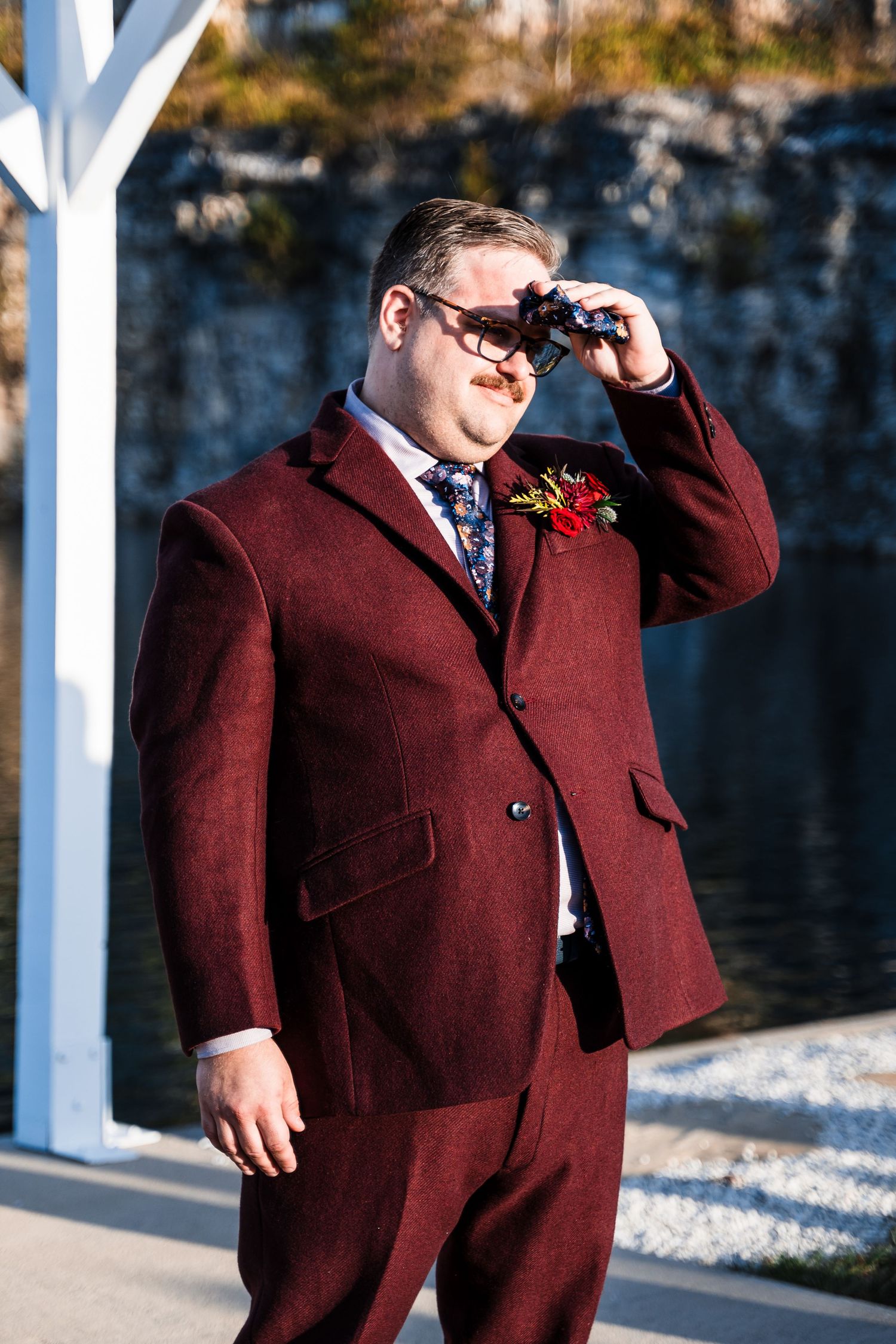 Person in a burgundy suit poses confidently against an outdoor backdrop.