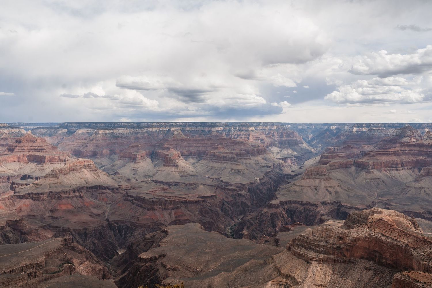 Dramatic view of the Grand Canyon's layered red rock formations under cloudy skies in Arizona.