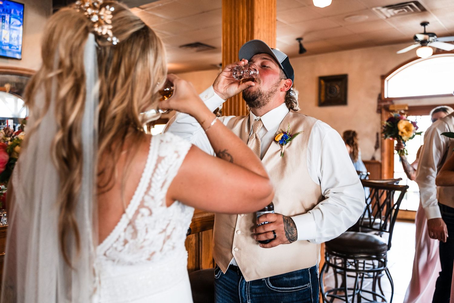 A couple shares a touching moment during their wedding celebration as they toast and raise their drink glasses together.
