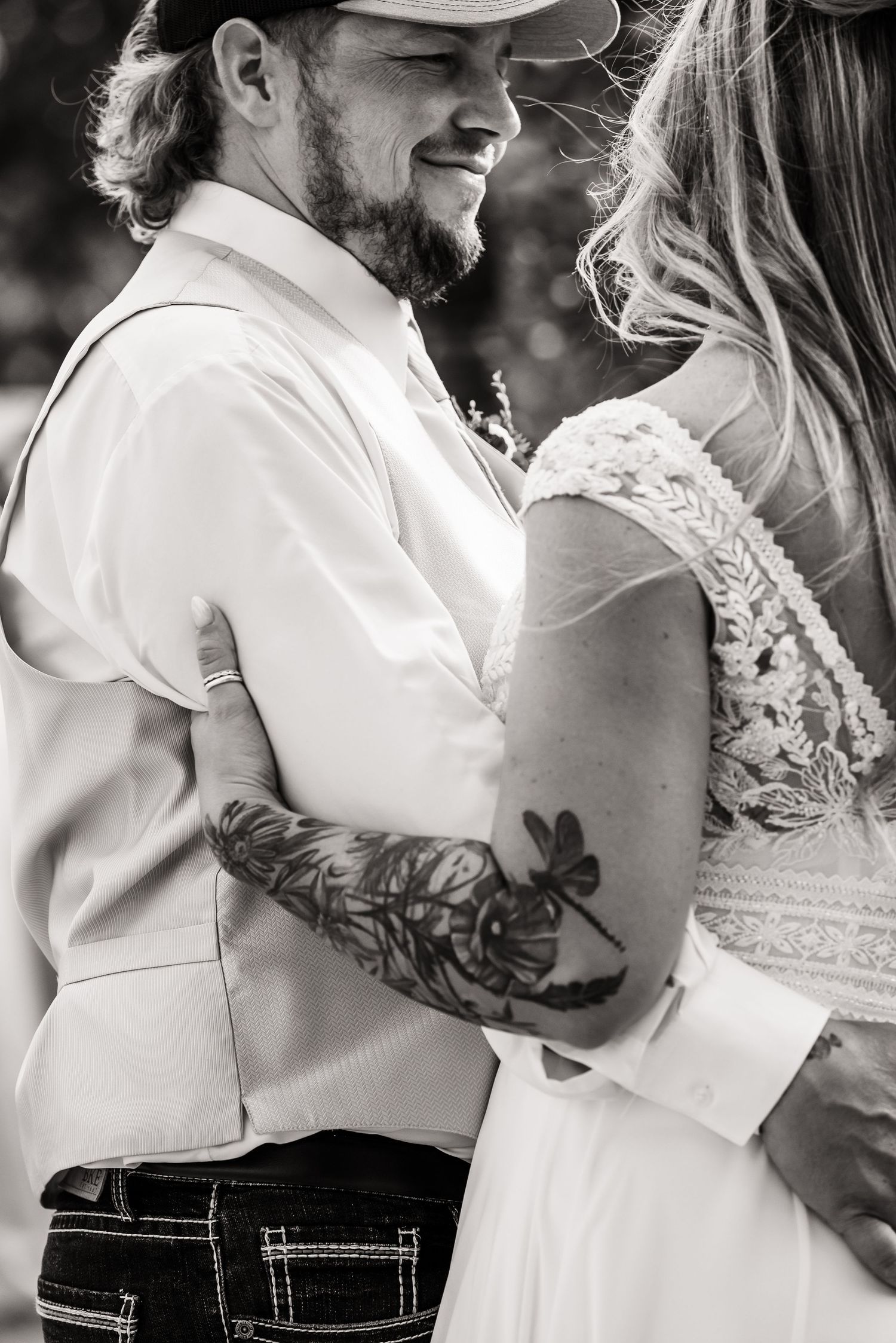 Black and white close-up of couple in wedding attire showing floral arm tattoo.