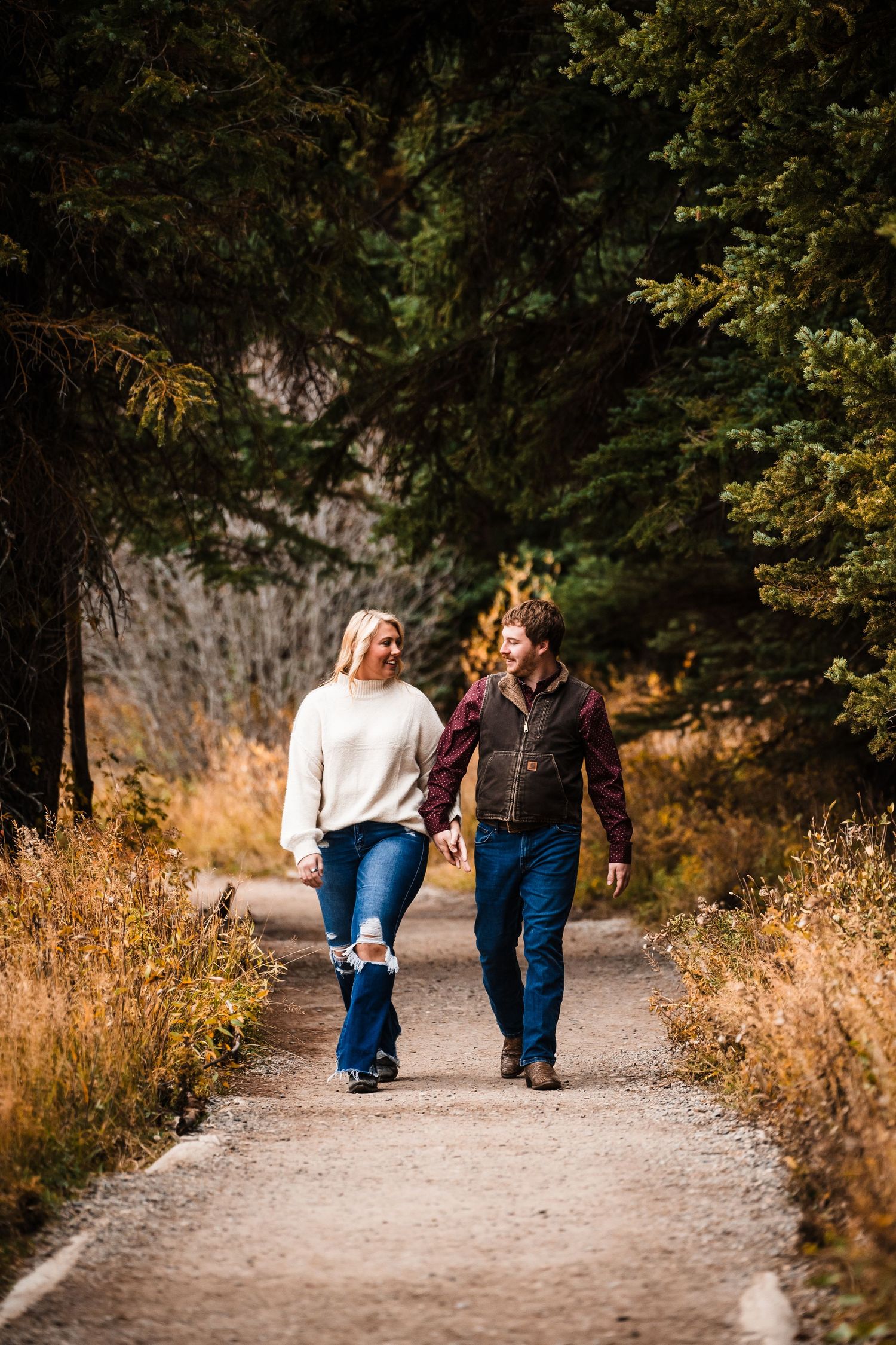Couple walking together on a scenic autumn trail surrounded by golden foliage.