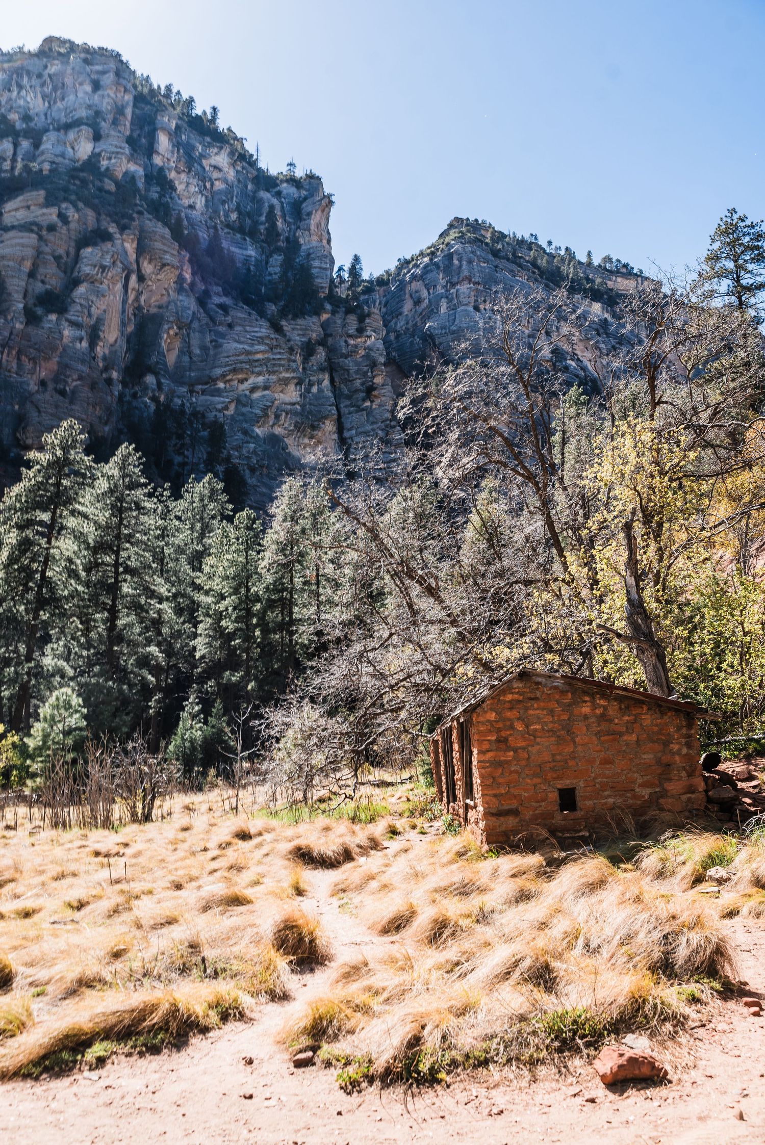 Rustic stone cabin nestled beneath towering limestone cliffs in a remote mountain valley.