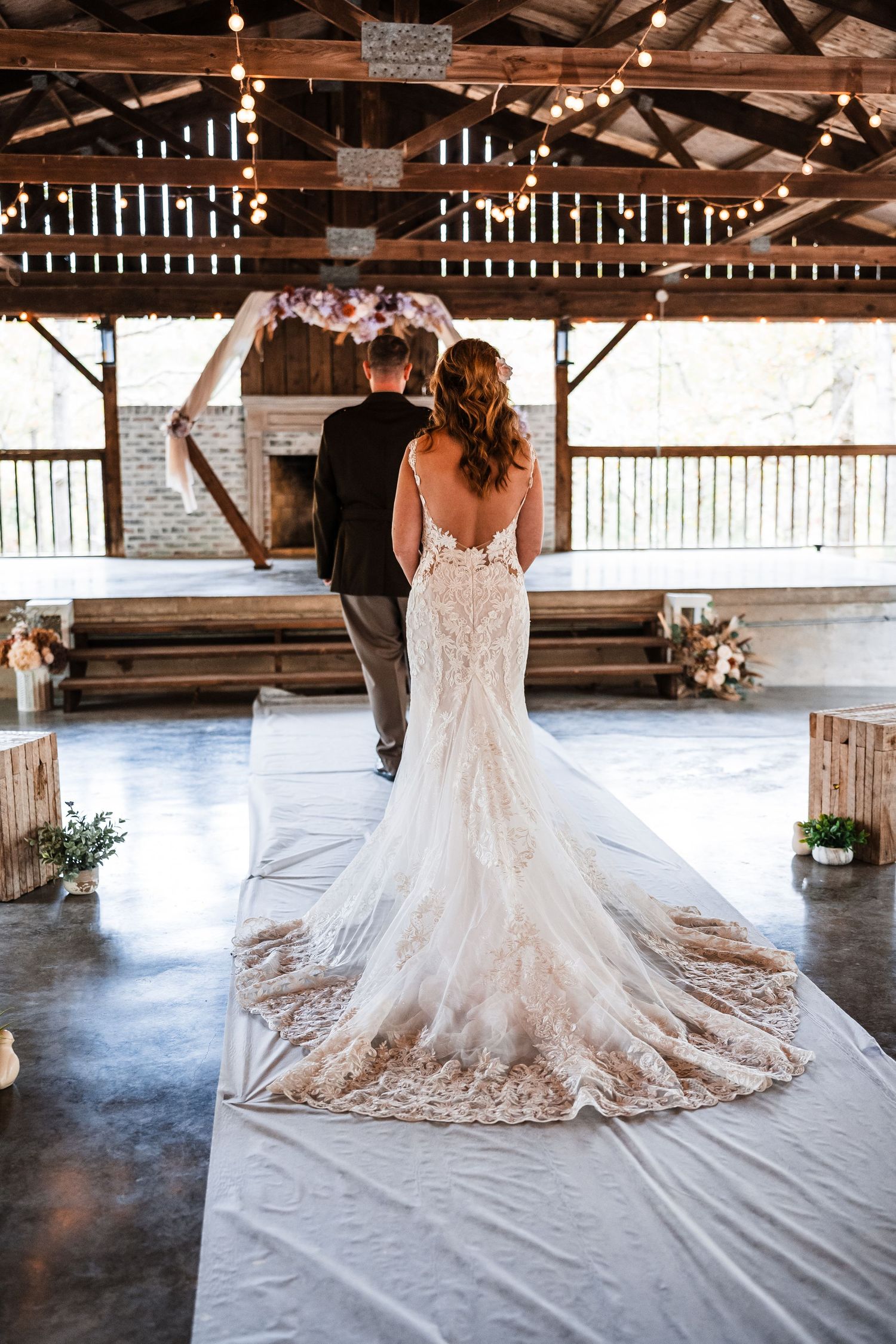Back view of a bride's lace wedding dress train spread out on a rustic barn floor.