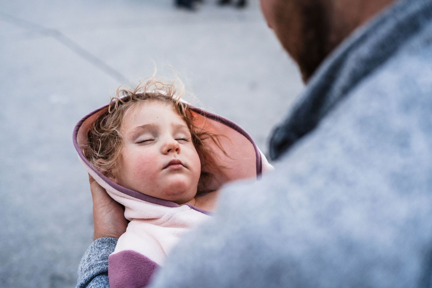 A sleeping child in pink clothing is gently cradled in someone's hands against a blurred background.