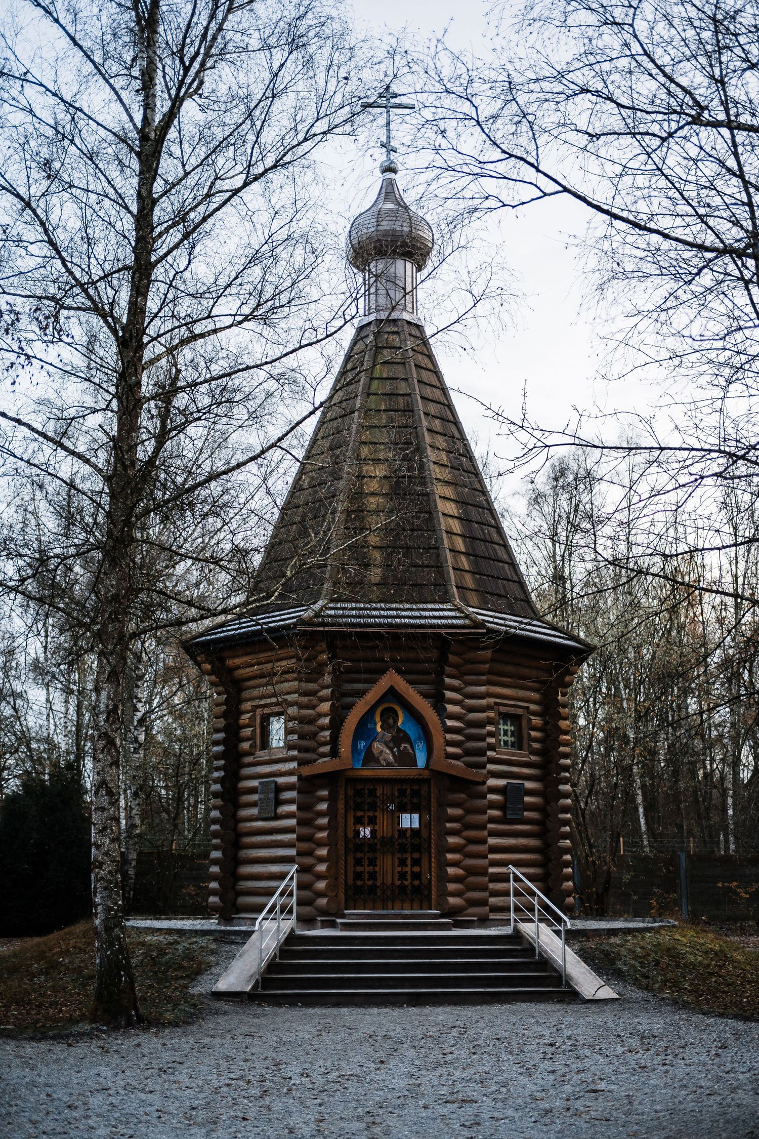 Rustic wooden Orthodox church with striped log walls and onion dome stands in a snowy winter forest setting.
