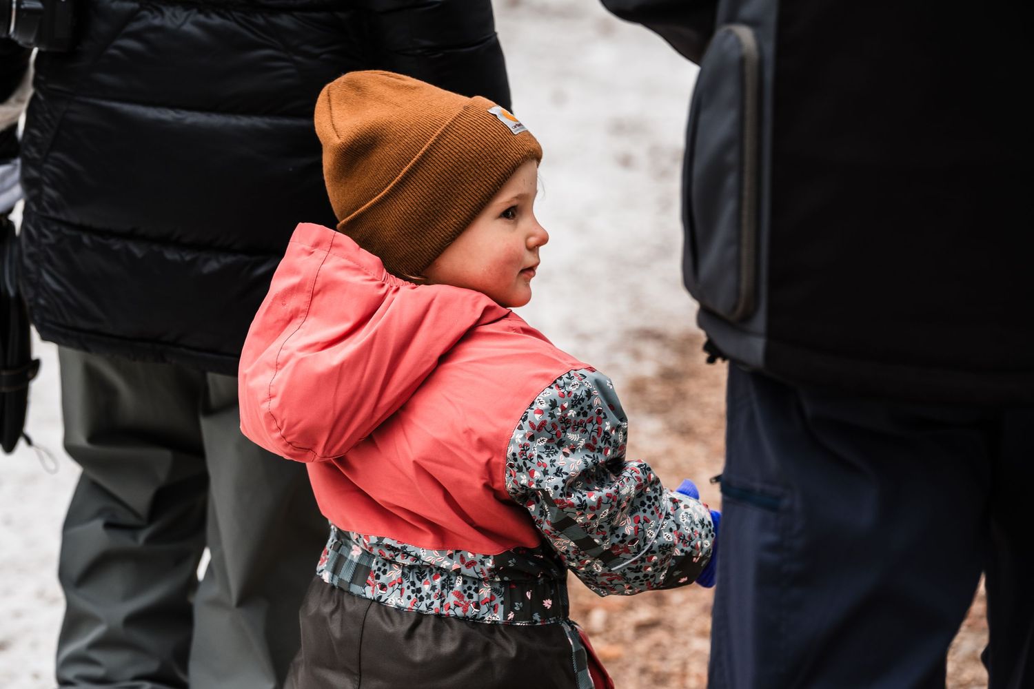 A person wearing a brown beanie and pink winter coat walks along a snowy path in winter.
