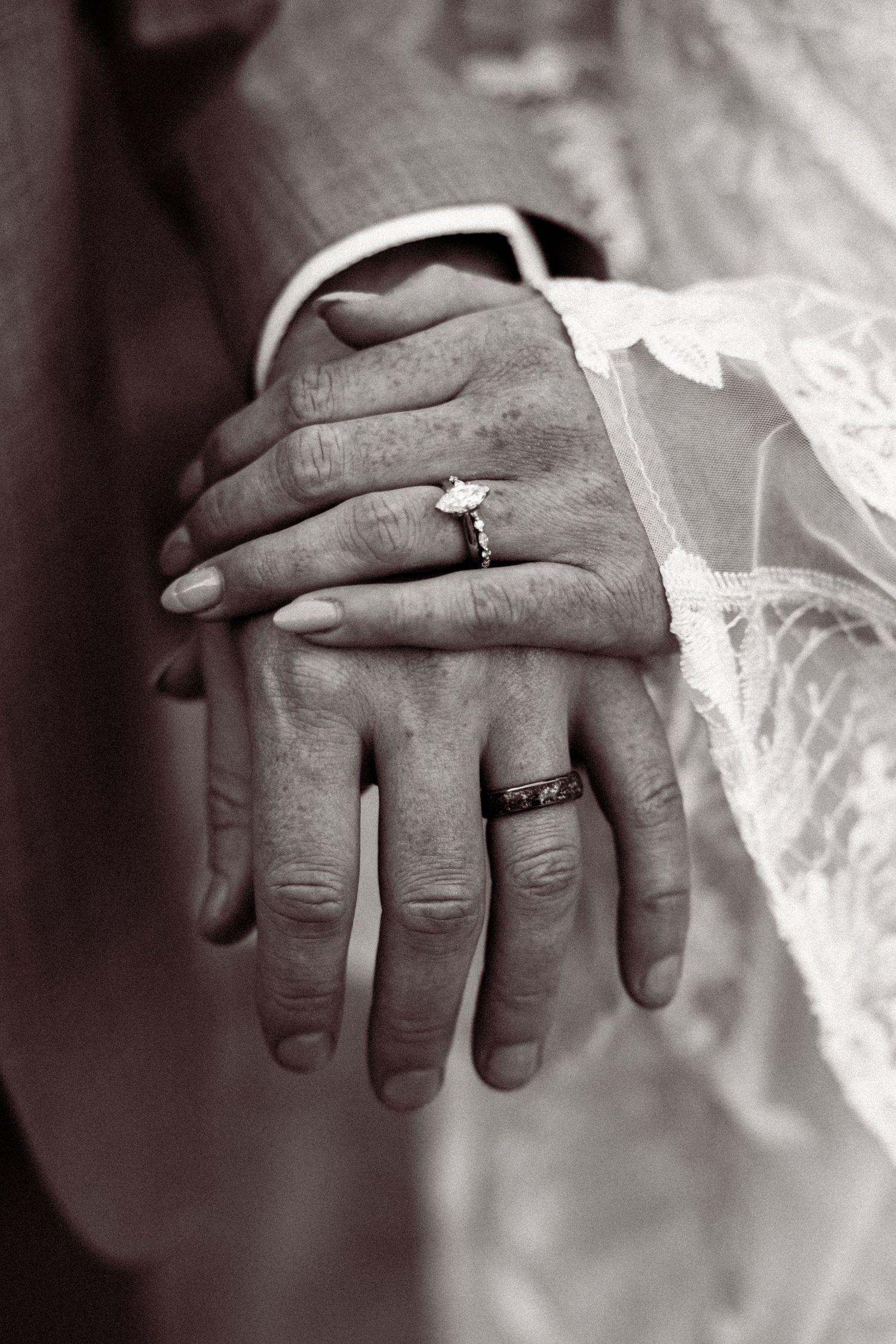 Close-up black and white photo of newlyweds hands showing diamond engagement ring and wedding band.