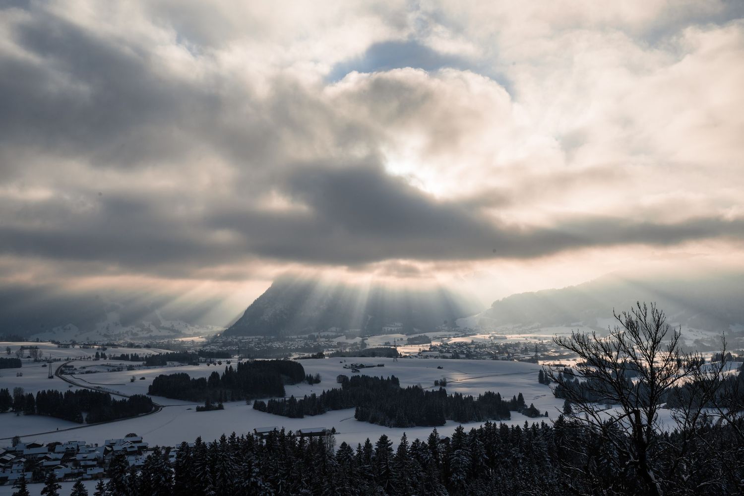 Dramatic sunbeams pierce through clouds over a snow-covered winter landscape.