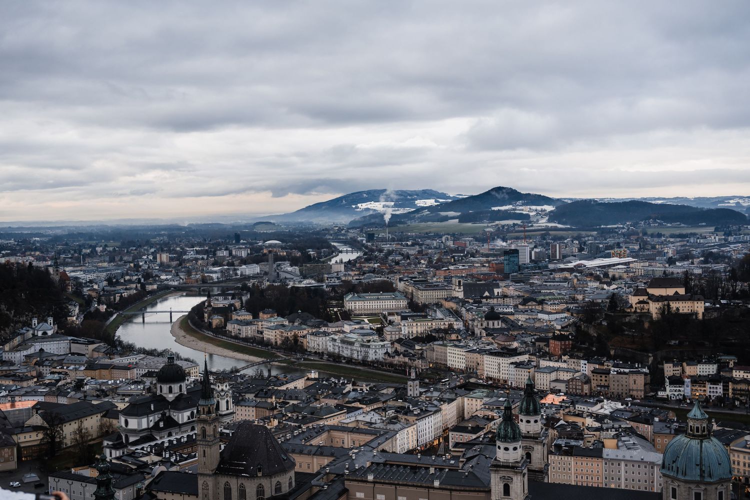 Panoramic cityscape view of Salzburg with river, buildings and mountains in winter.