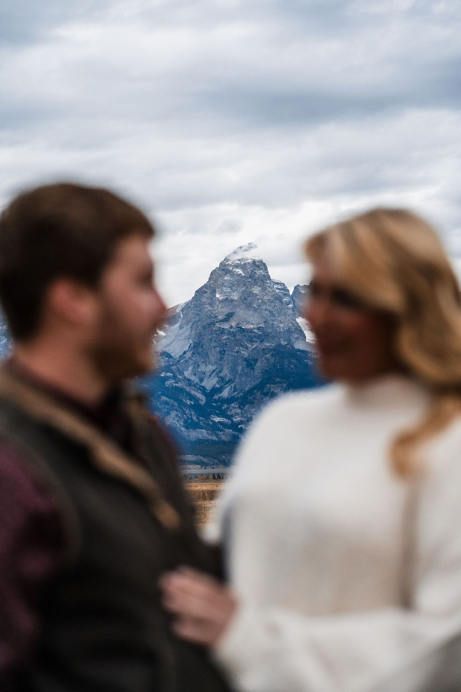A couple shares an intimate moment against a dramatic mountain backdrop in Grand Teton National Park.