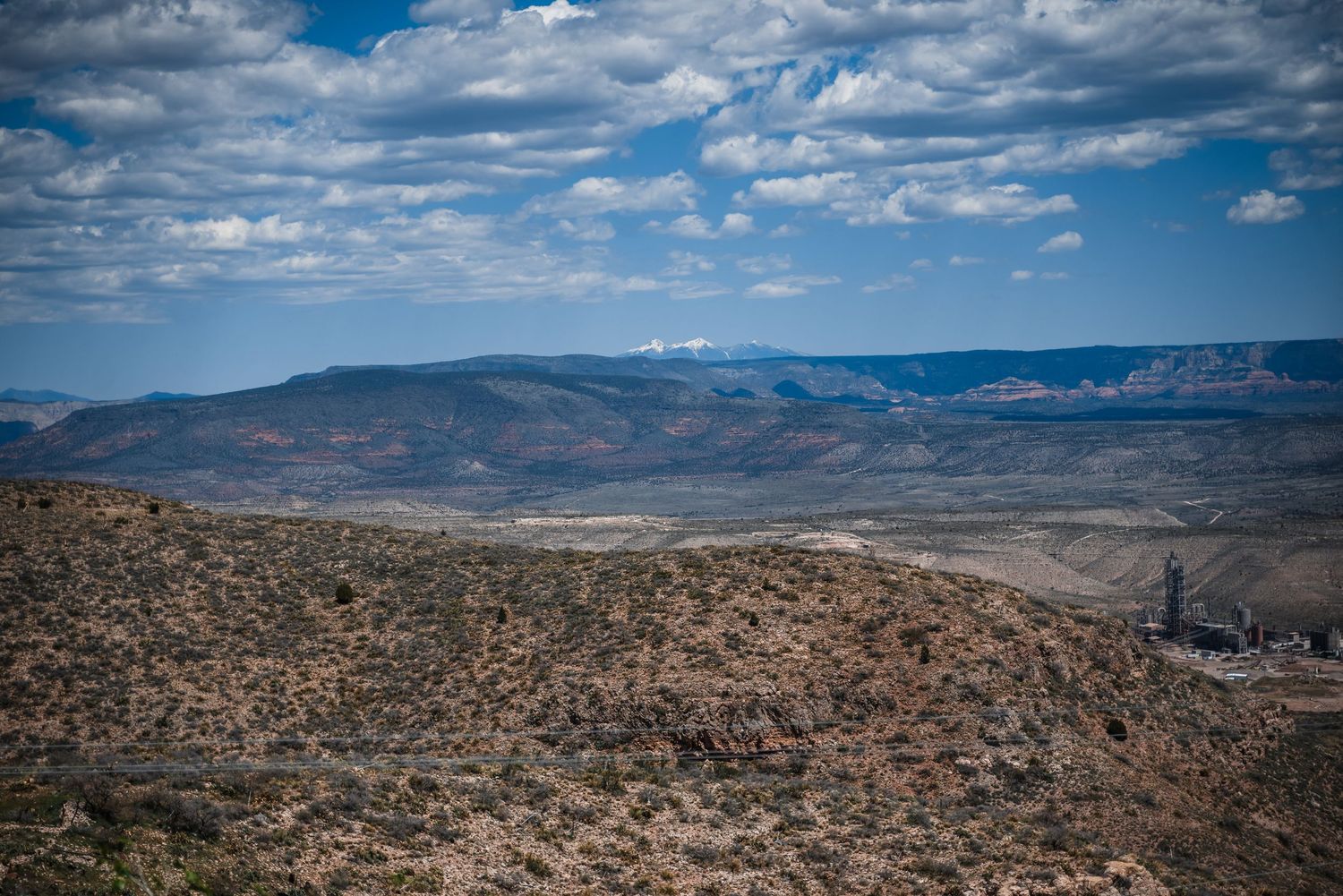 Dramatic desert landscape with rolling hills and mountains under a blue sky with scattered puffy clouds.