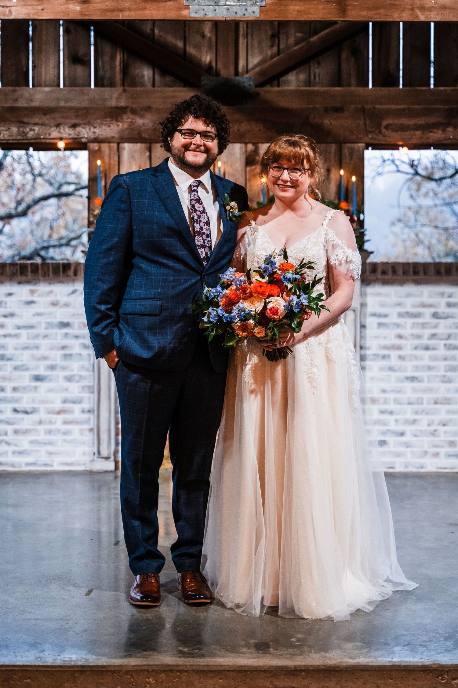 Newlyweds pose for formal portrait in rustic barn venue with string lights.