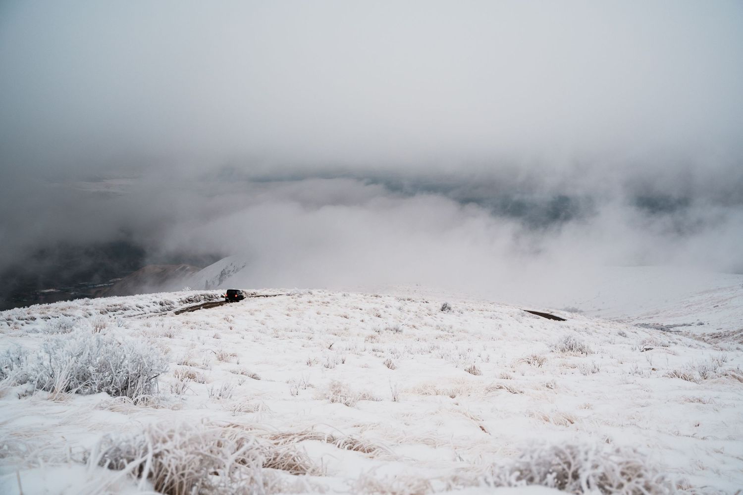 A misty winter landscape with snow covered ground and foggy mountains in the distance.