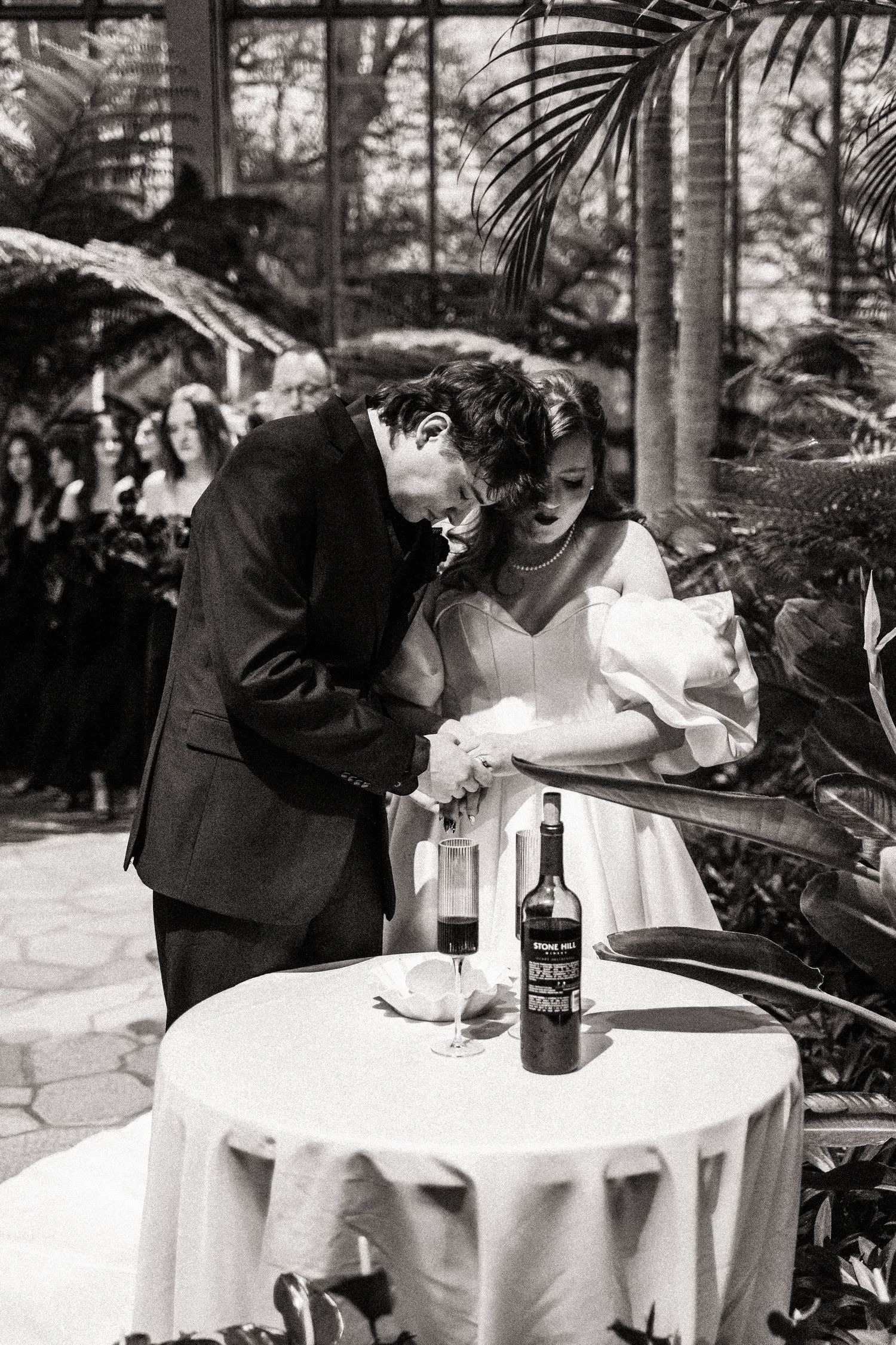 Wedding couple sharing an intimate moment at a small table with wine during their ceremony.