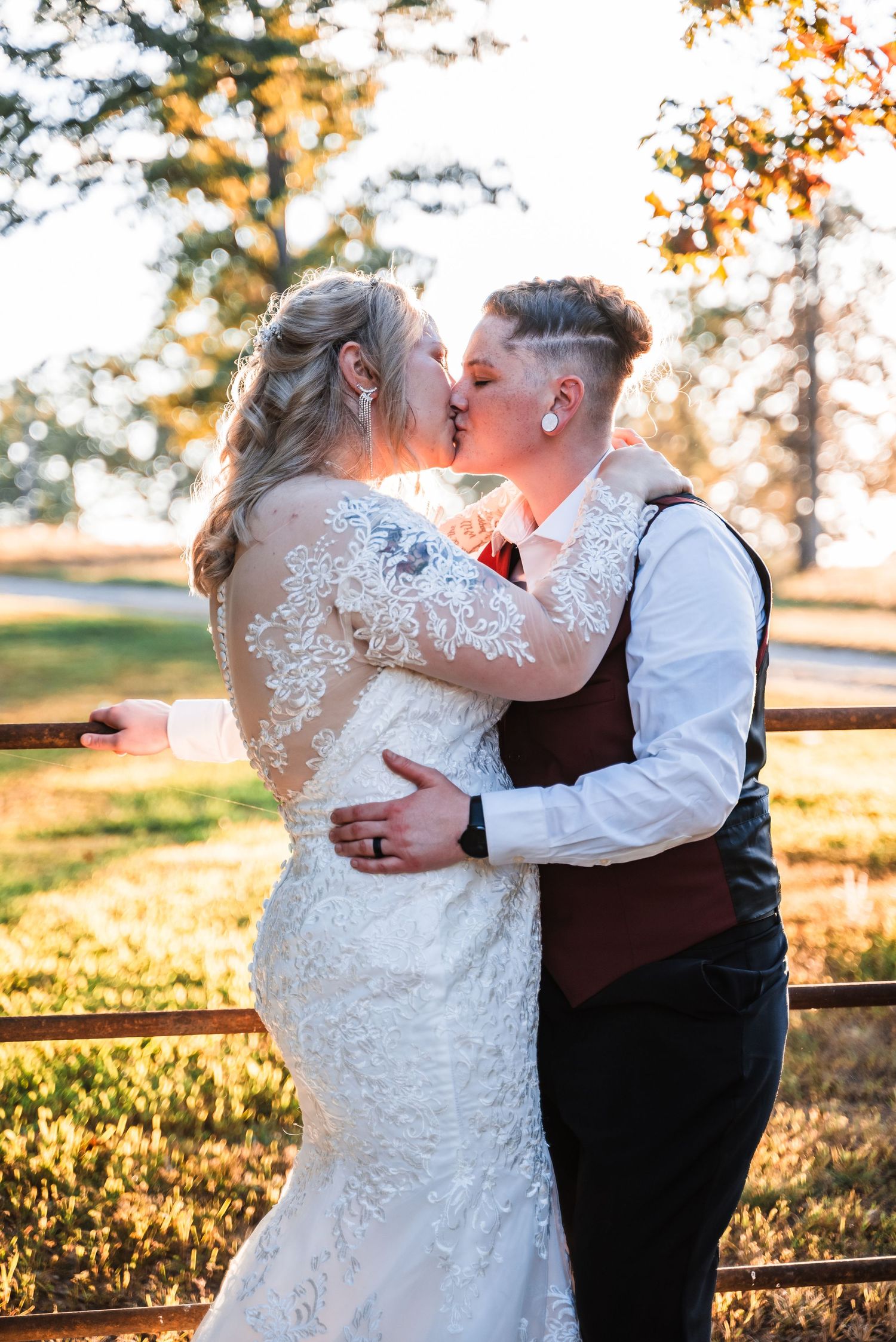 A romantic golden hour wedding portrait shows a couple kissing against a rustic fence backdrop in autumn.