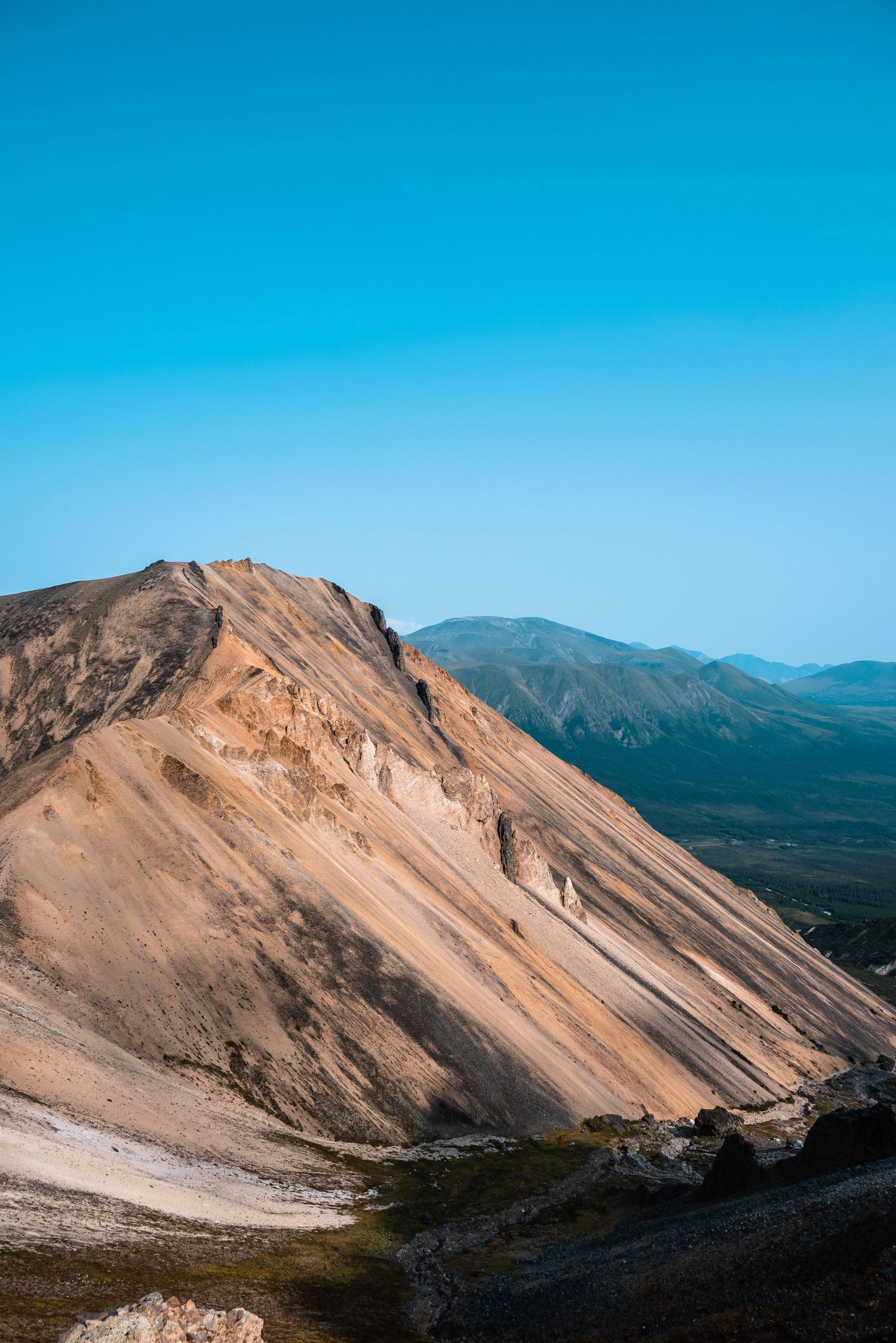 Rugged mountain peak with golden slopes rises against vibrant blue sky in a dramatic desert landscape.