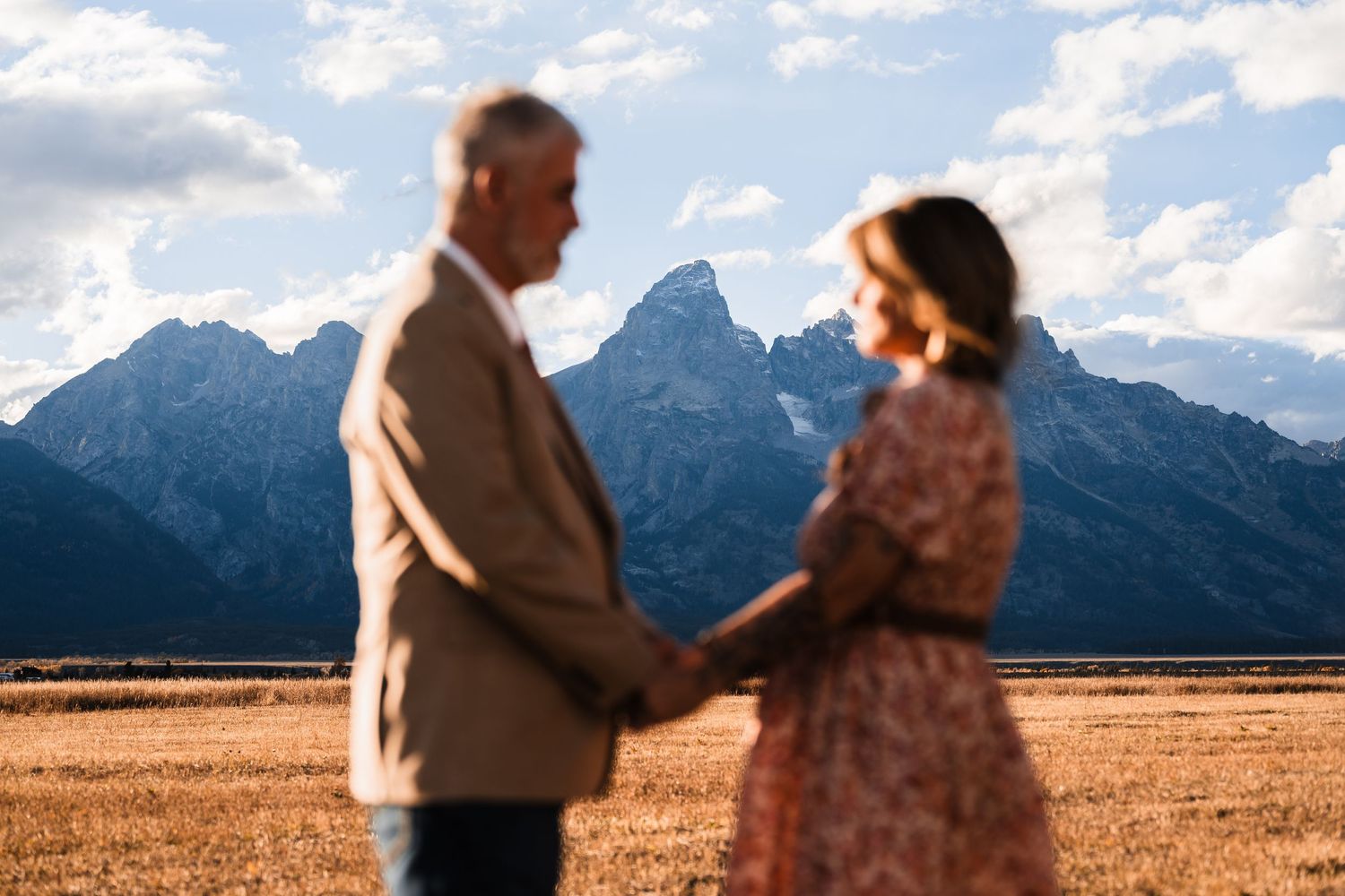 Two people stand together against a backdrop of majestic mountain peaks in Grand Teton National Park.