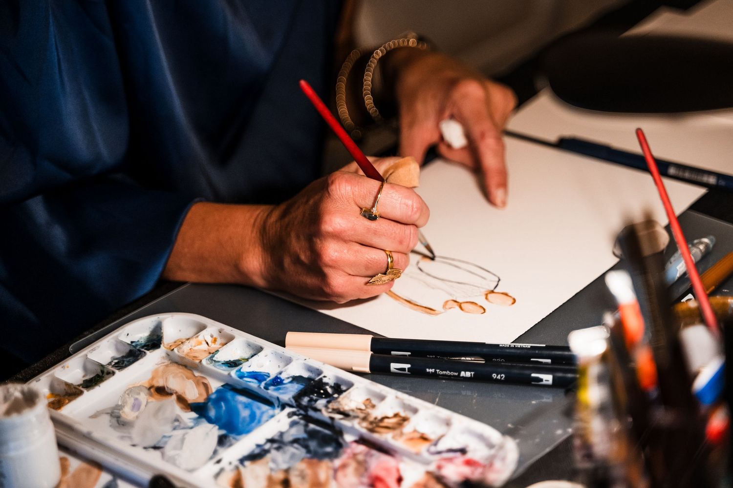 Close-up shots of hands drawing and painting with art supplies on a dark surface.