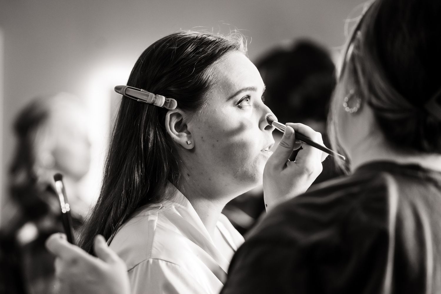 Black and white photo of makeup application during wedding preparations.
