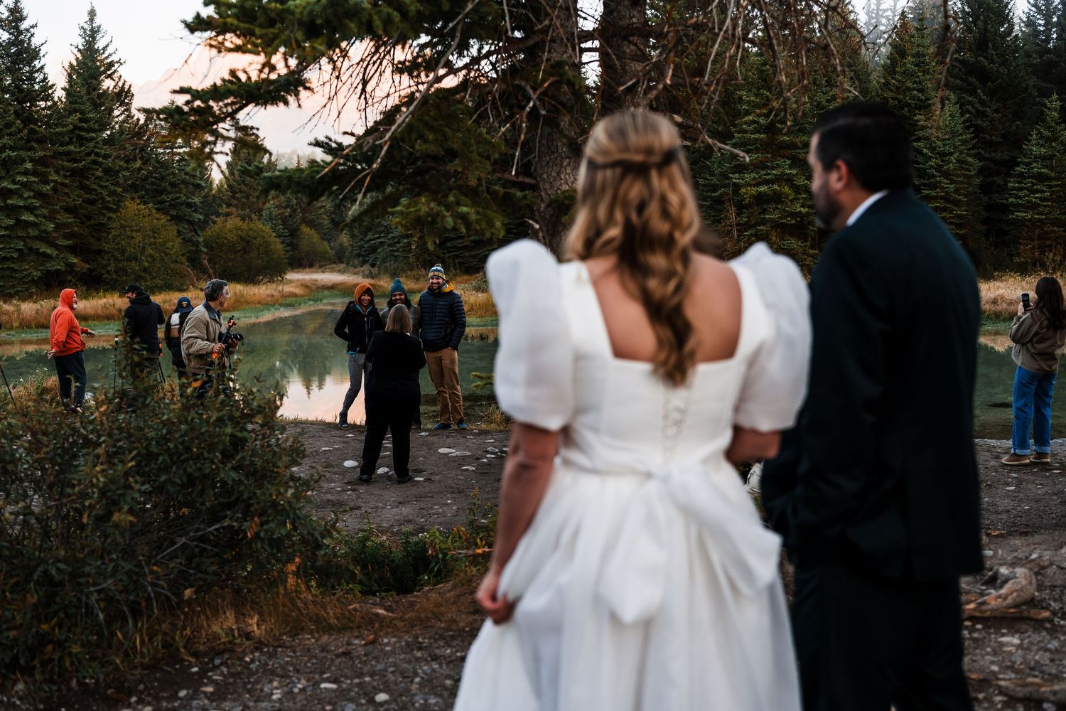 A romantic wedding couple poses among evergreen trees during golden hour in a mountain setting.
