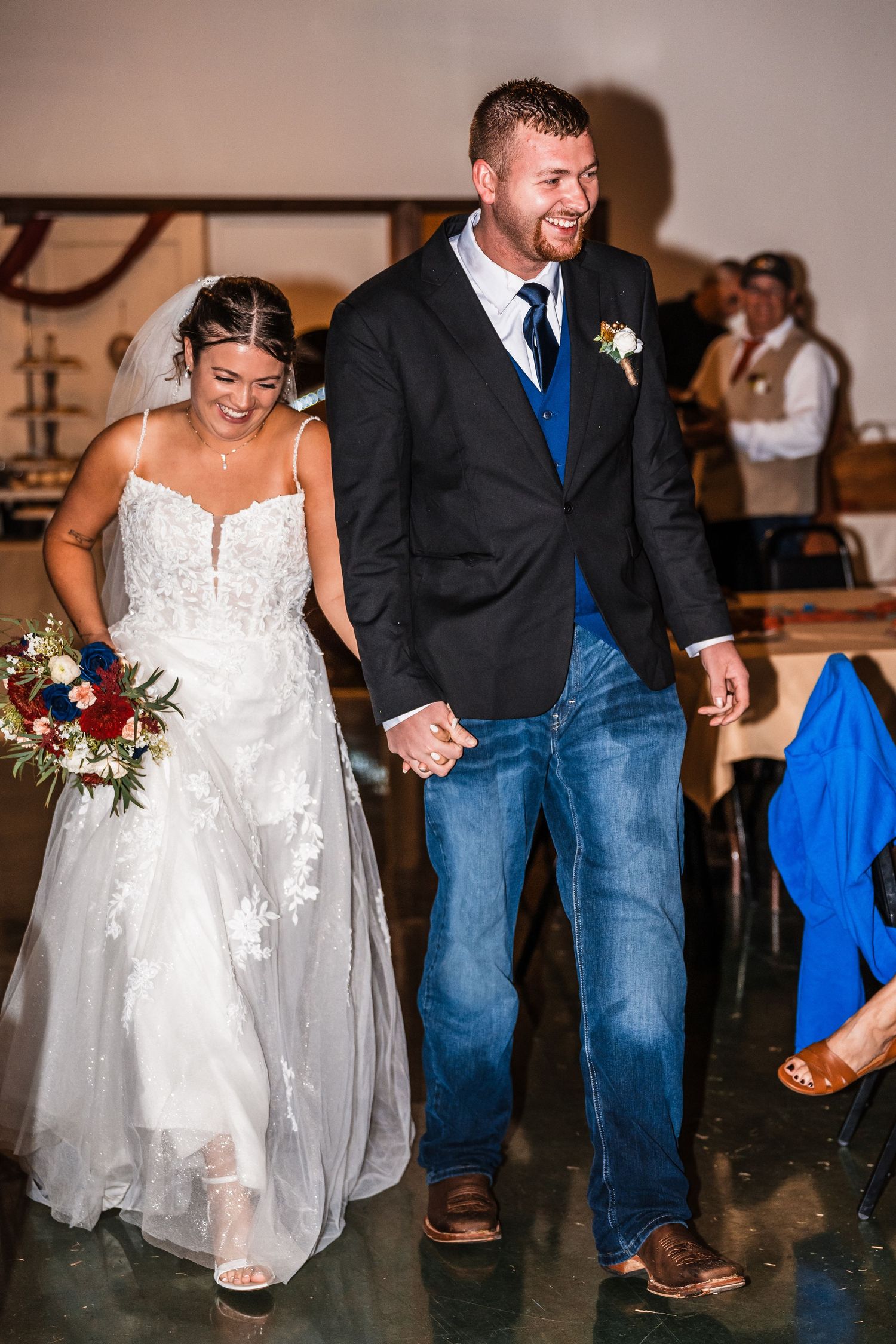 Couple walks together during wedding ceremony with rustic venue decor in background.