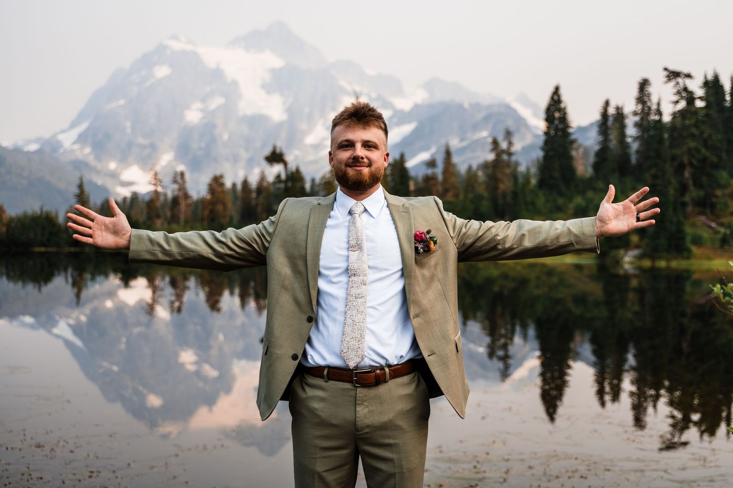 A scenic mountain wedding photo shoot with reflective lake and snow-capped peaks in the background.