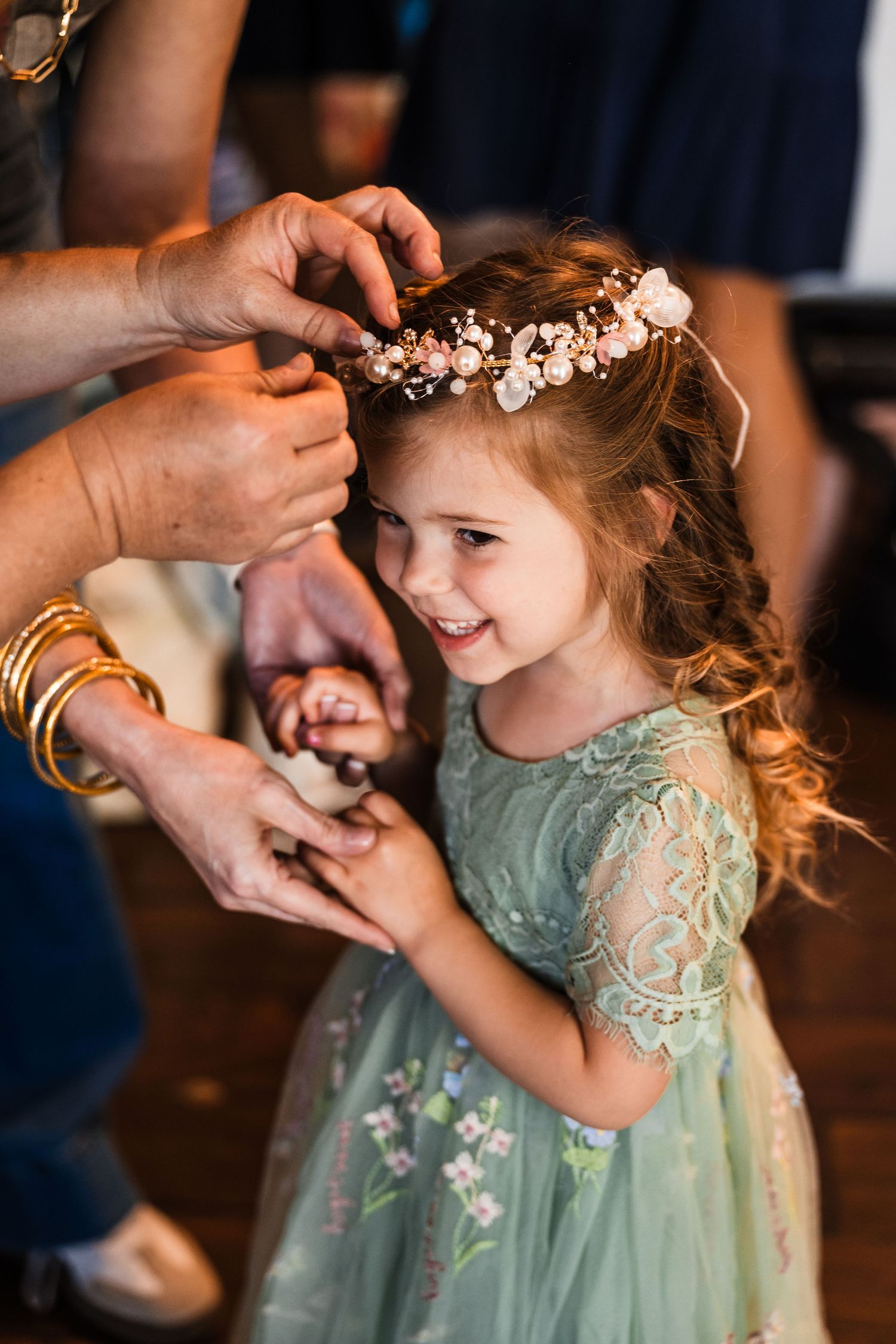 Adorable flower girl in mint green dress having floral crown placed on her curly hair.