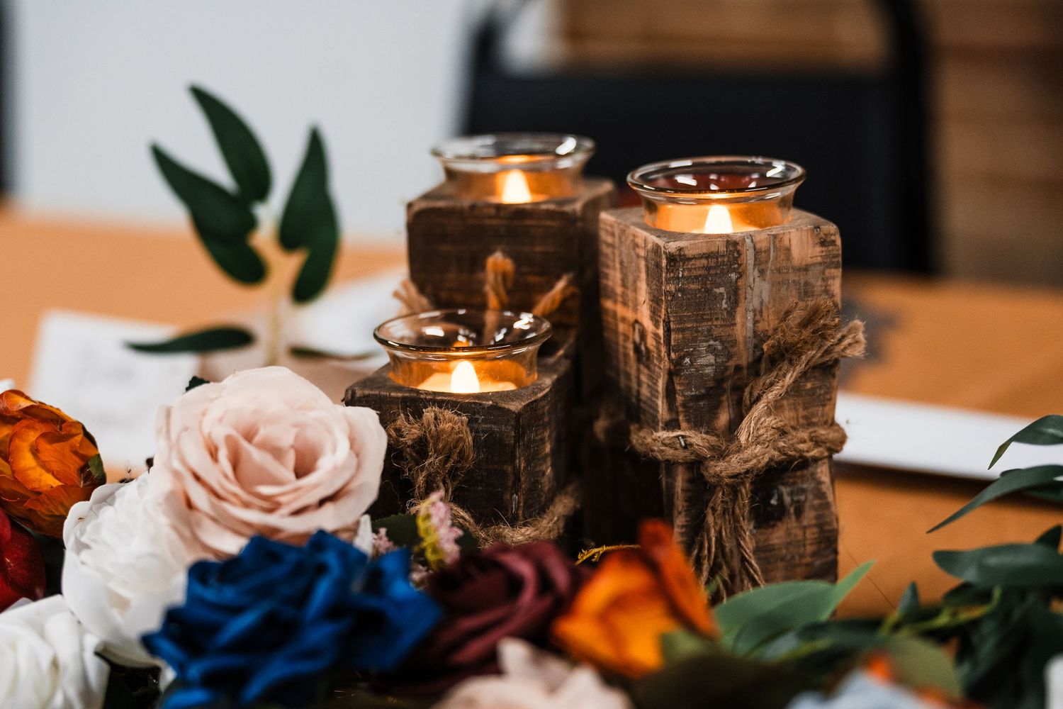 Wedding reception table decorated with glowing candles, blush roses and rustic wooden elements.