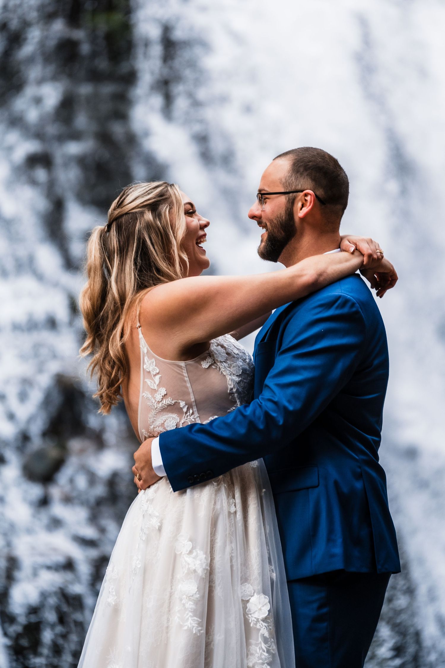 A romantic wedding couple shares intimate moments in front of a misty waterfall backdrop.