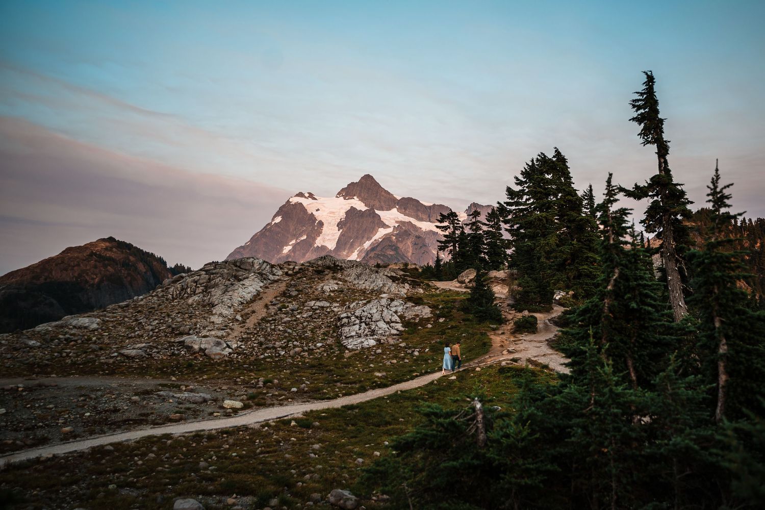 A winding trail leads through evergreen trees toward snow-capped Mount Baker during golden hour in Washington state.